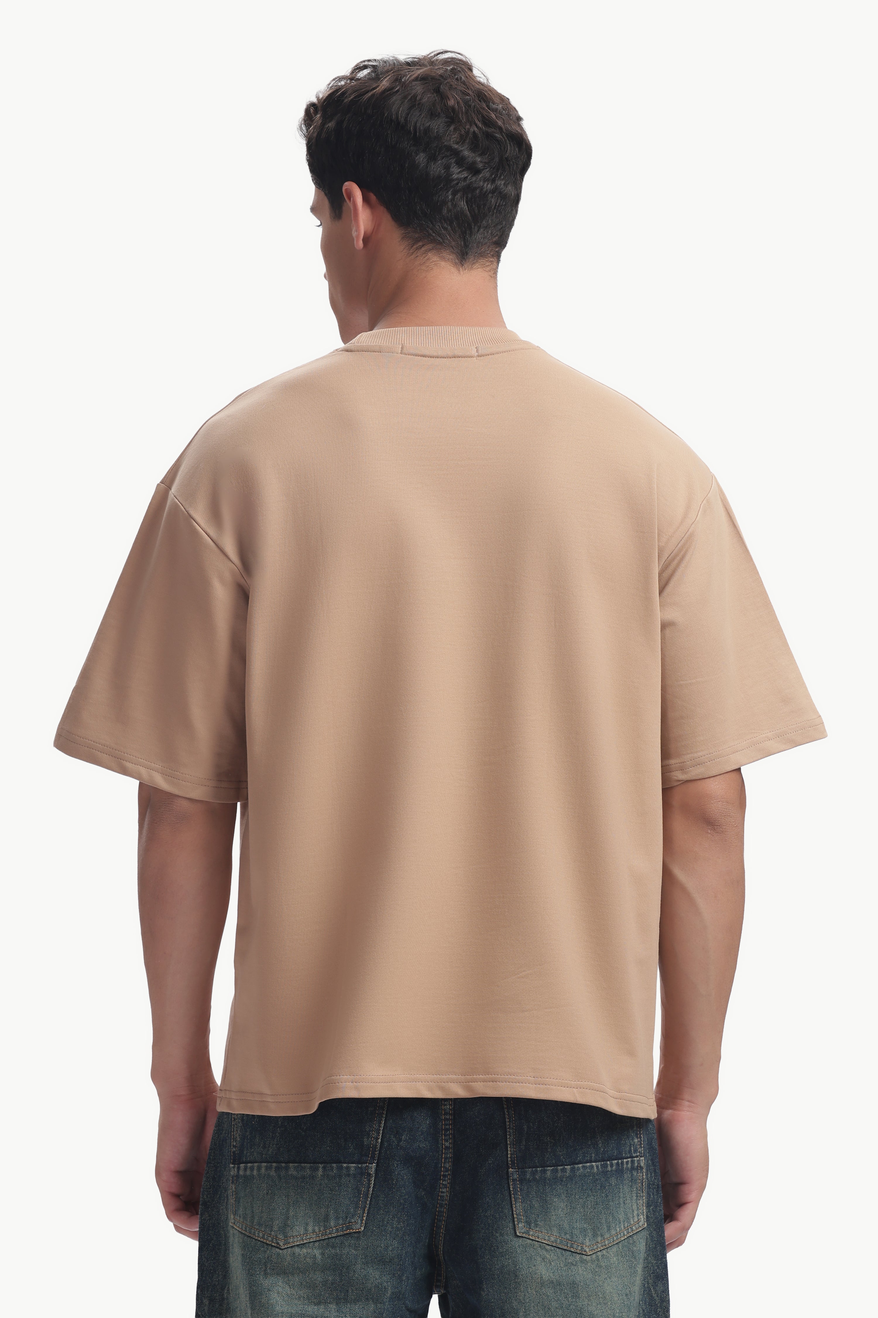 Man wearing a beige Oversized Fit Focal Point T-Shirt from the back, showcasing its relaxed silhouette.