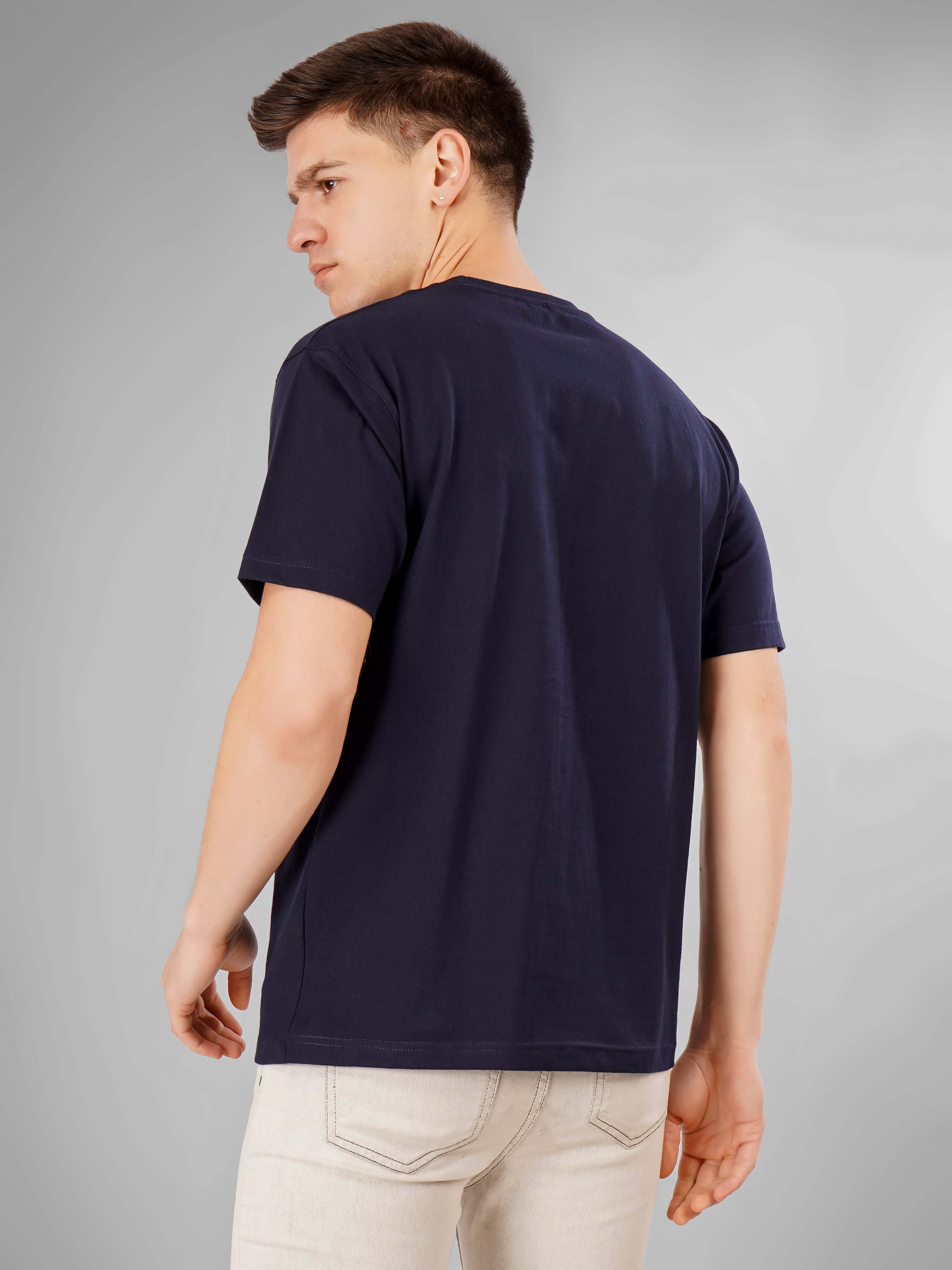Man wearing Solid Logo for Men a navy blue D'Cavros T-shirt with a bold white printed logo on the chest, paired with light gray jeans, posing confidently against a plain grey background.