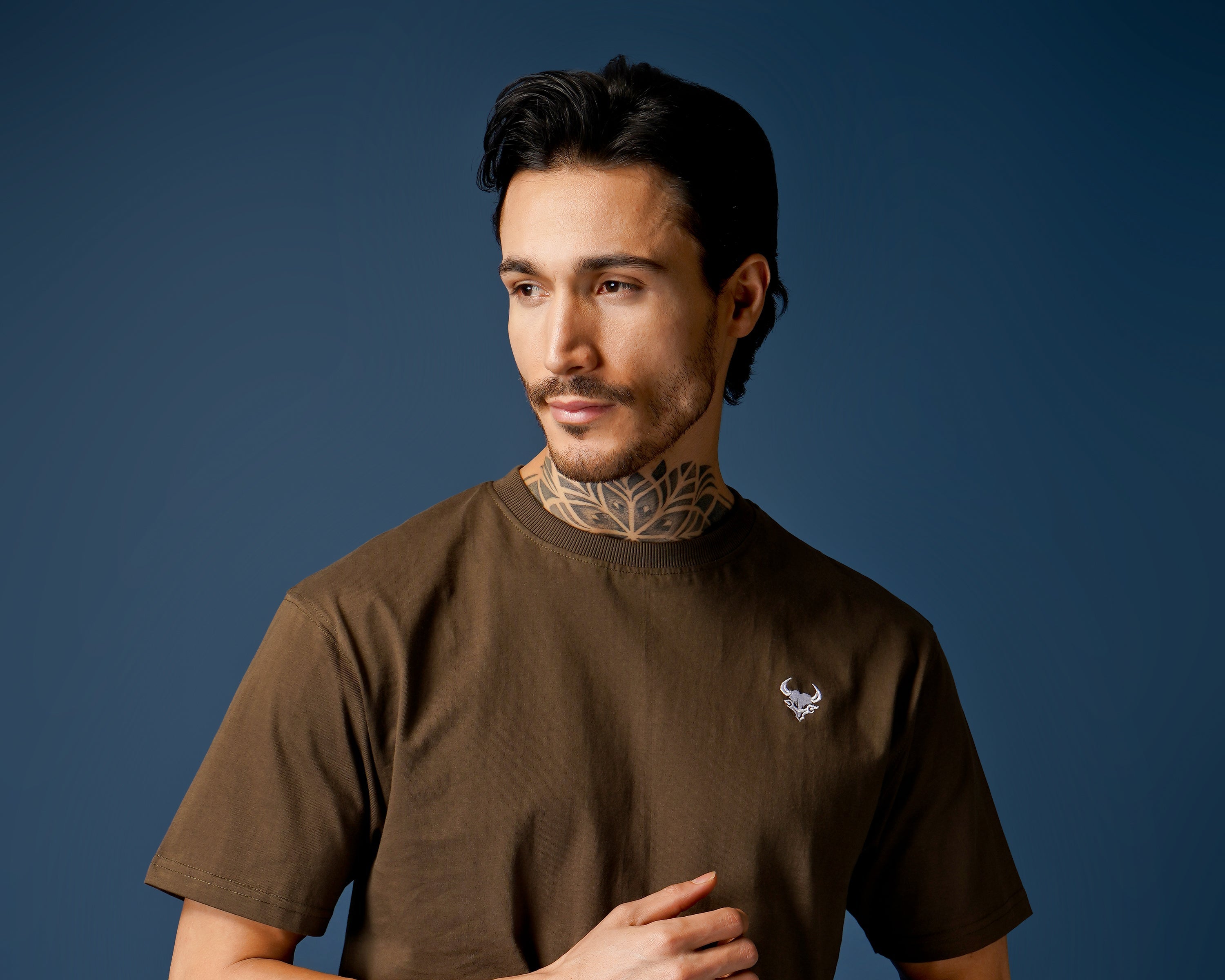 Man wearing a brown dcavros t-shirt against a blue background
