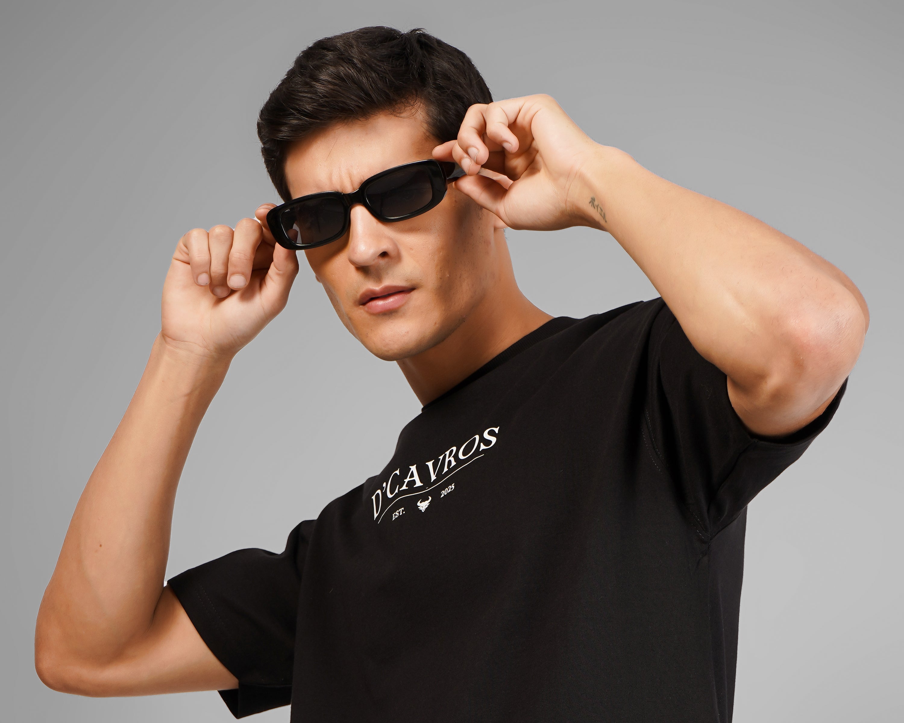 a person wearing black dcavros t shirt with sunglasses on gray background.