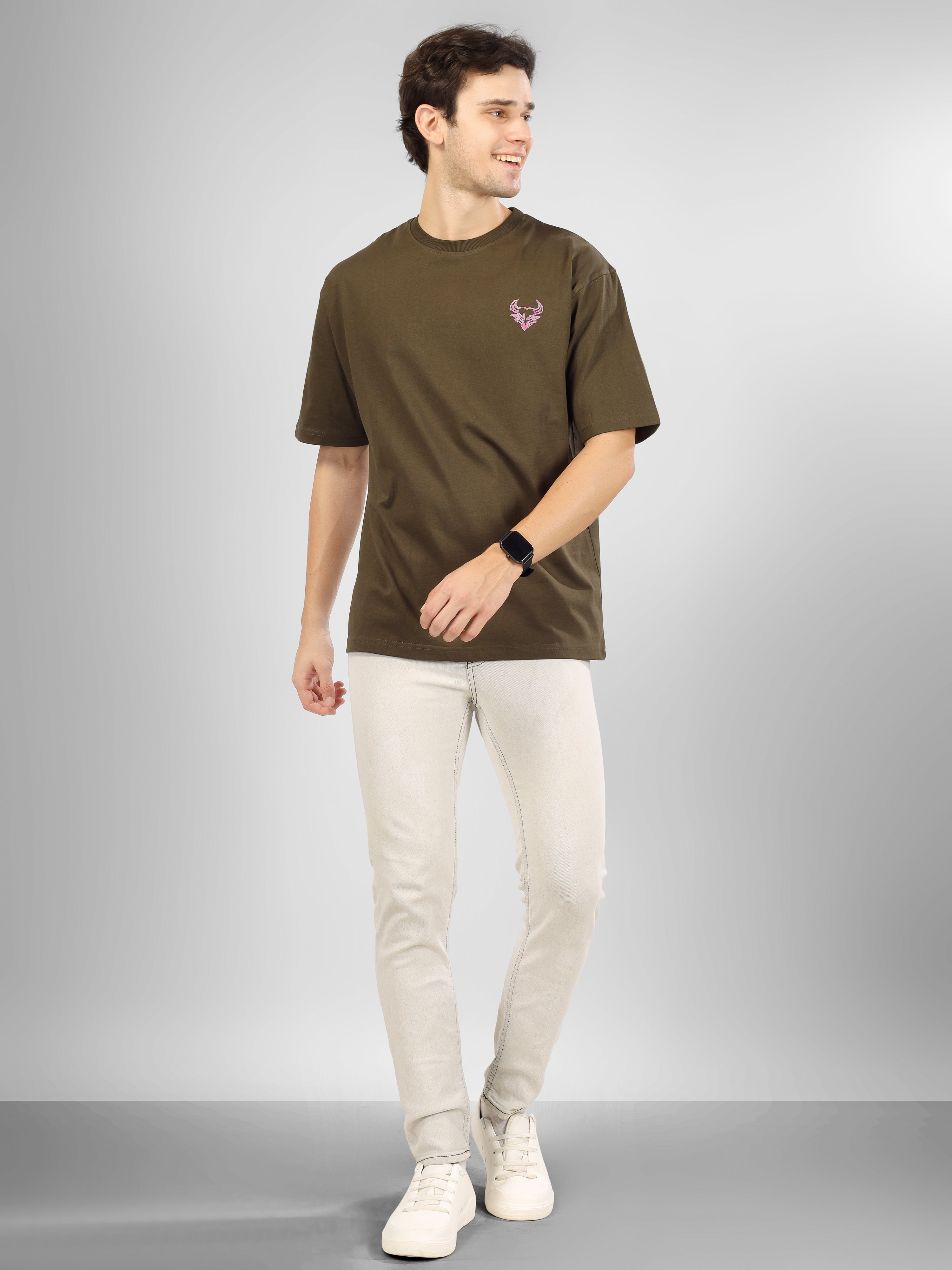 Man wearing olive green oversized D'Cavros T-shirt featuring a vibrant bull graphic and repeated D'Cavros logo text on the back, styled with beige jeans and sneakers.