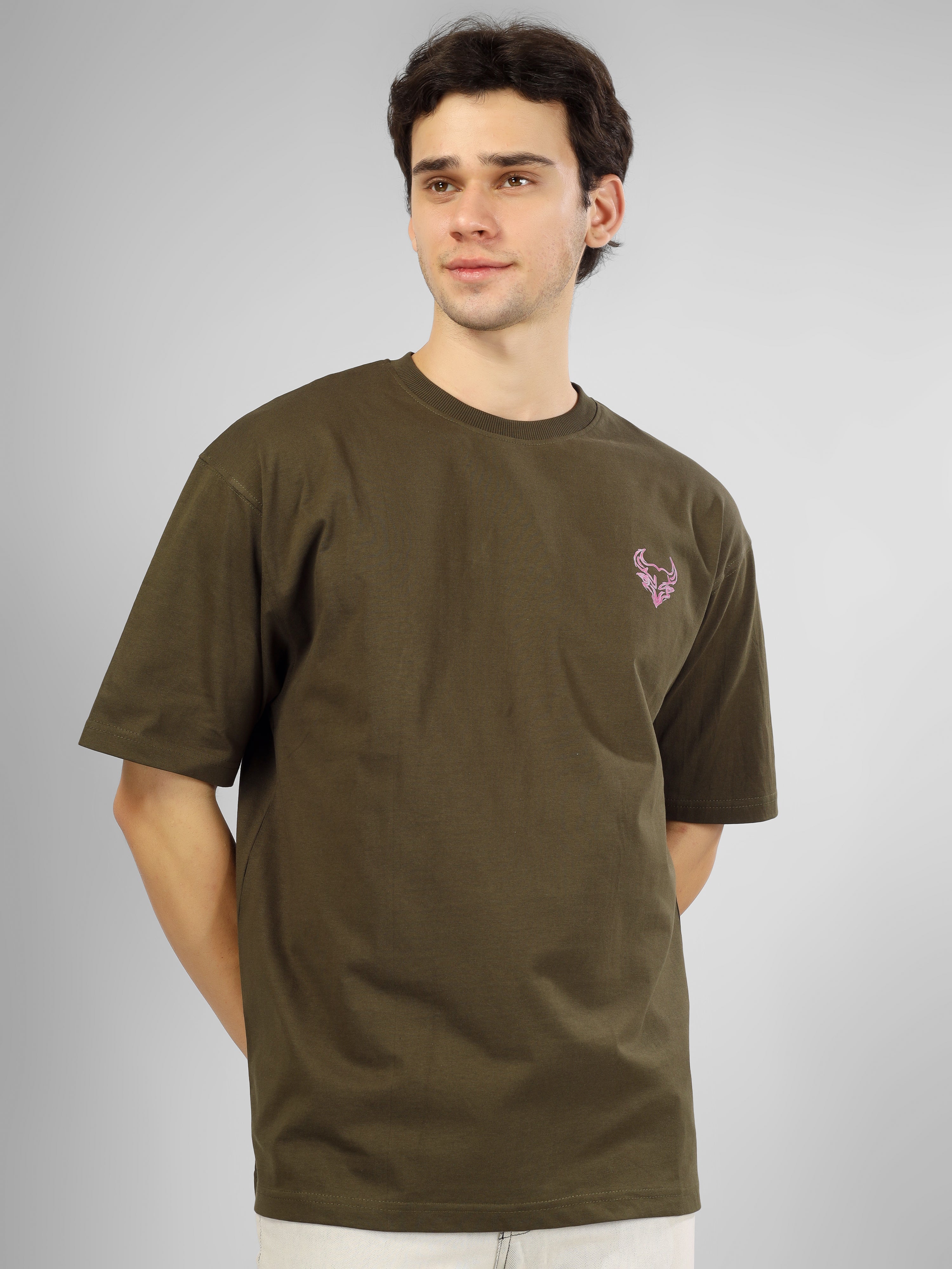 Man wearing olive green oversized D'Cavros T-shirt featuring a vibrant bull graphic and repeated D'Cavros logo text on the back, styled with beige jeans and sneakers.