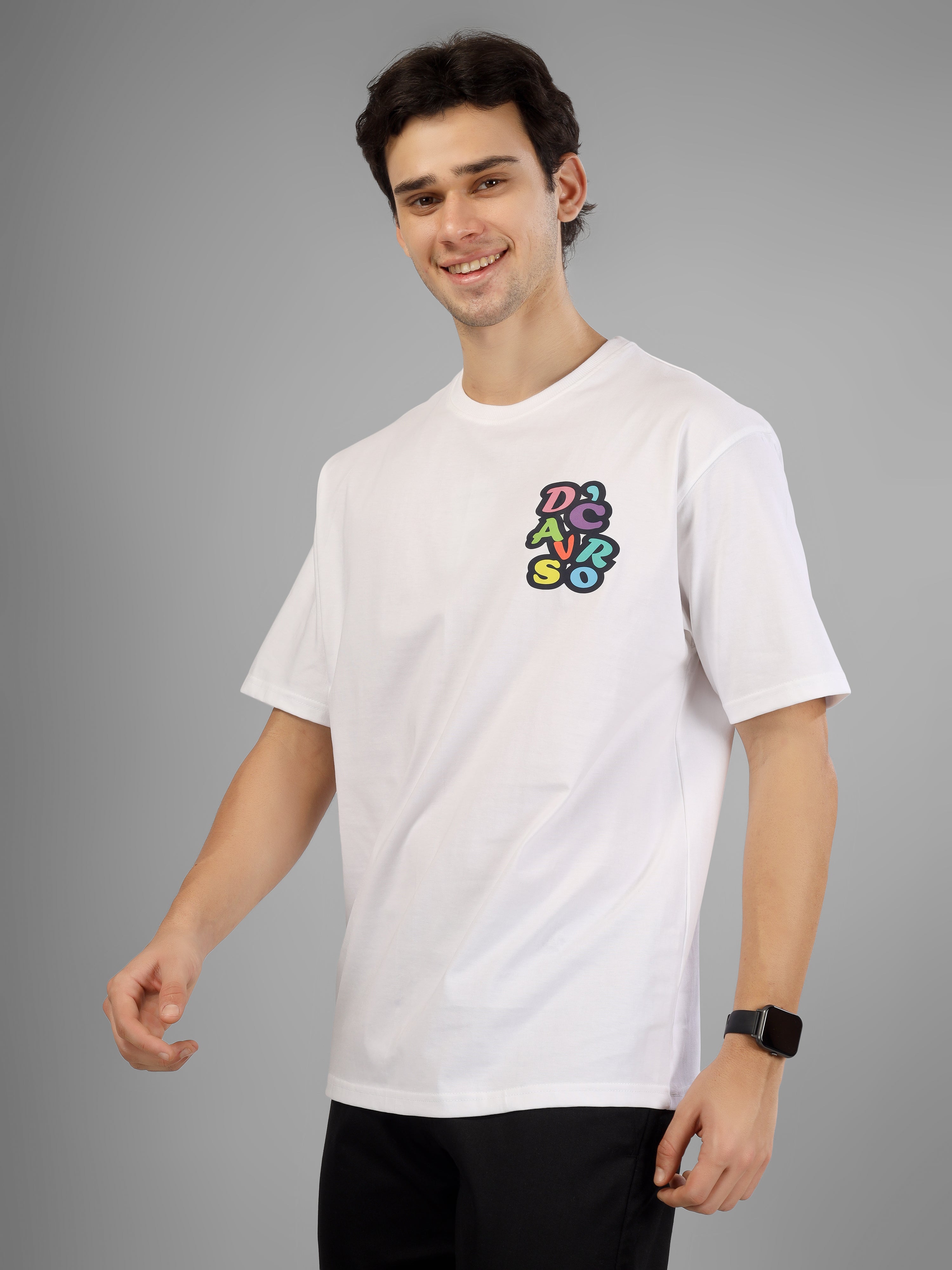 Male model wearing a white oversized dcavros T-shirt with a multicolor graphic logo on the left chest, styled with black pants and sunglasses.