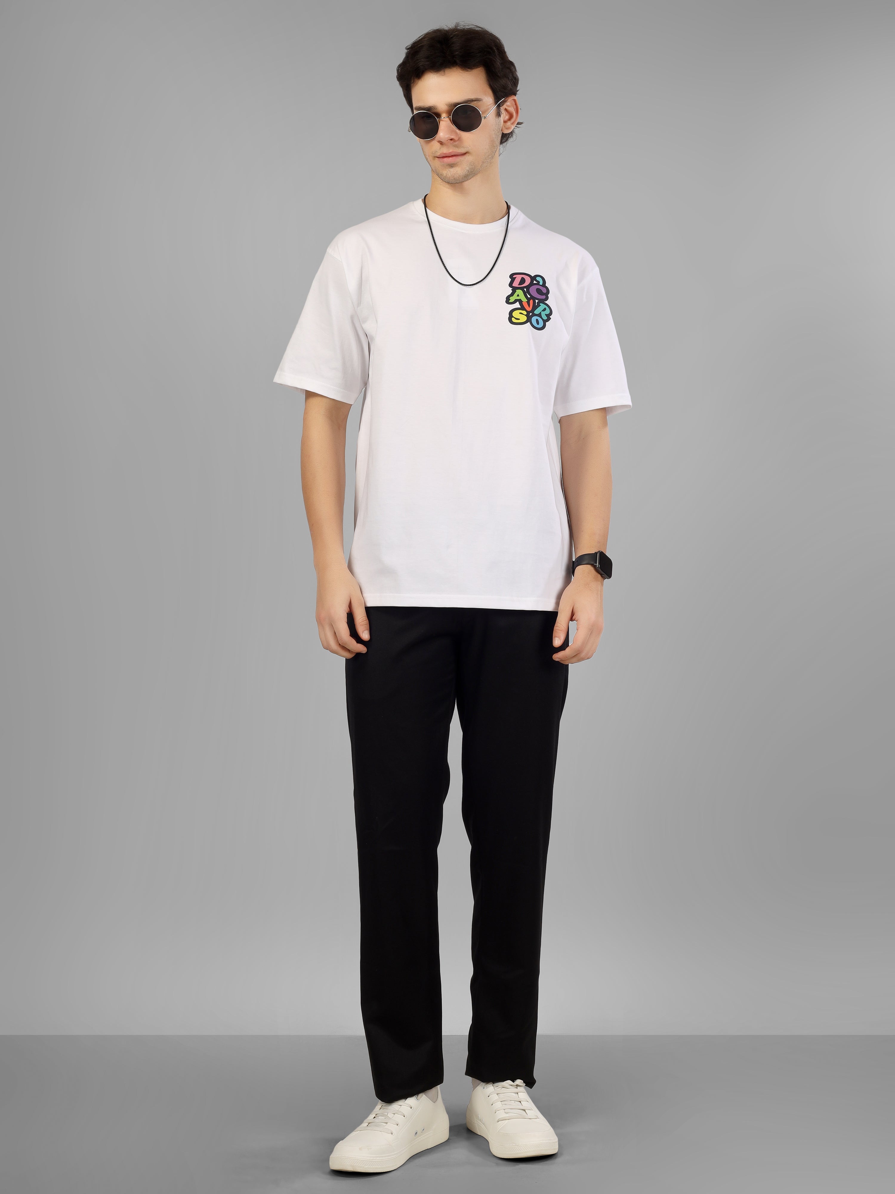 Male model wearing a white oversized dcavros T-shirt with a multicolor graphic logo on the left chest, styled with black pants and sunglasses.
