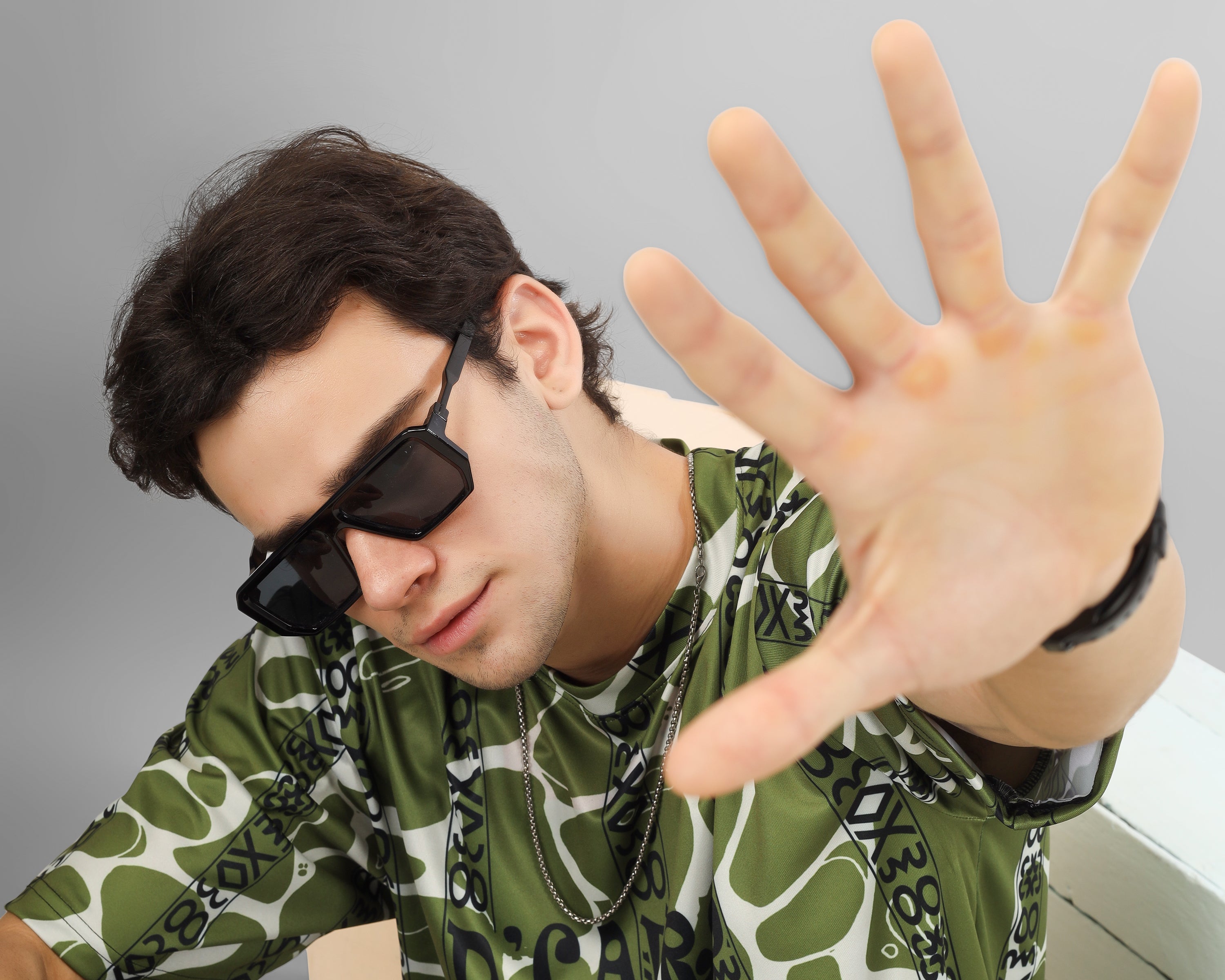 Person wearing a green patterned dcavros tshirt and sunglasses, making a stop gesture with their hand.