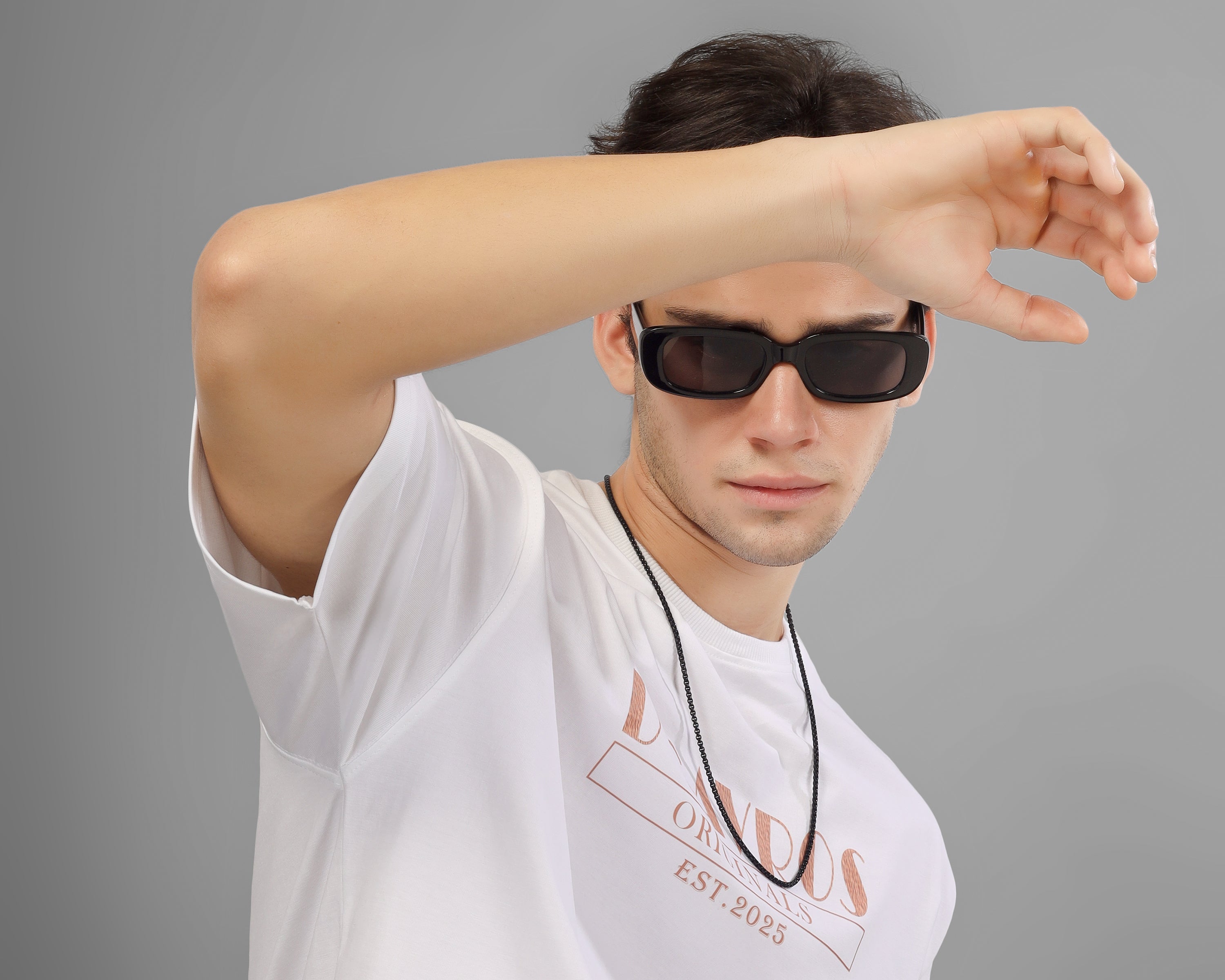 Person wearing a white dcavros t-shirt with text and black sunglasses on a gray background