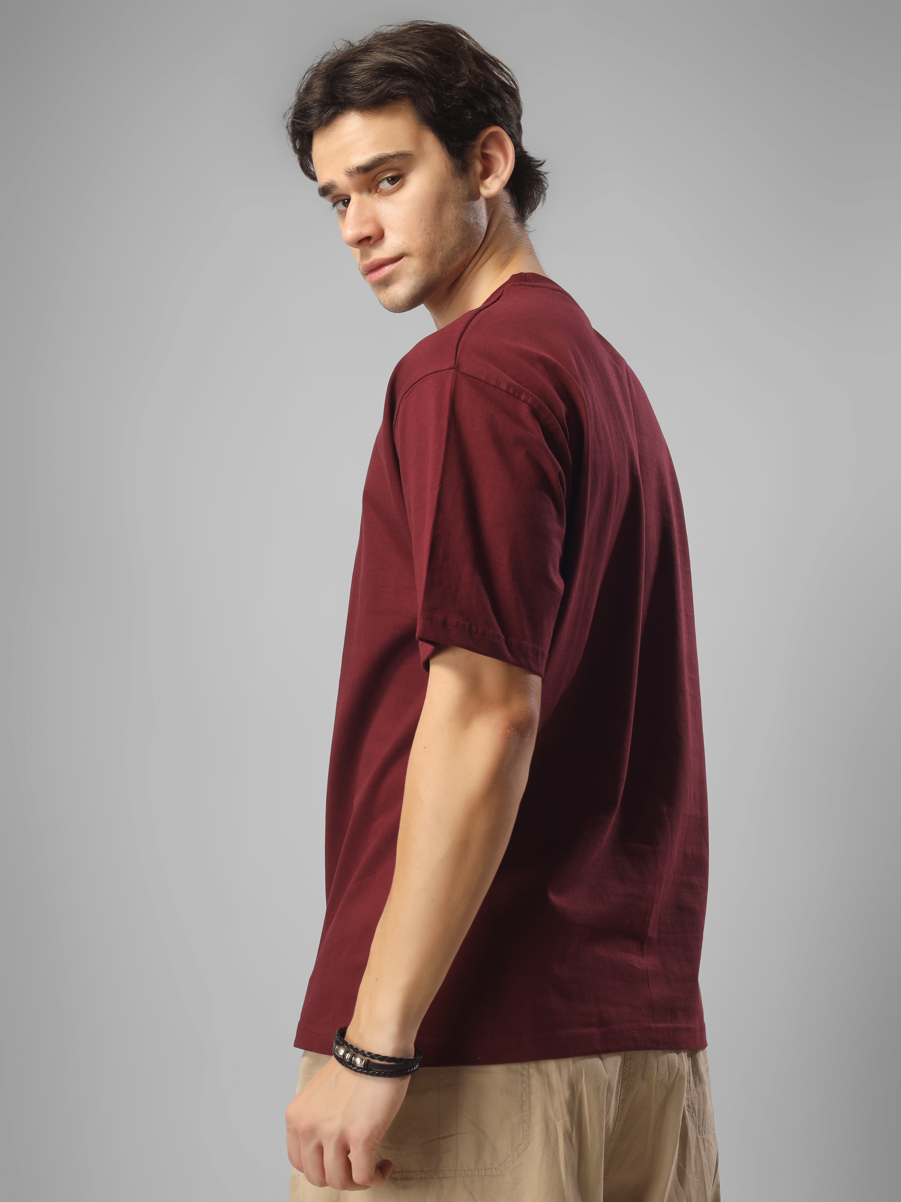 Male model wearing a maroon dcavros T-shirt featuring a black-and-white abstract center logo print, paired with beige pants.