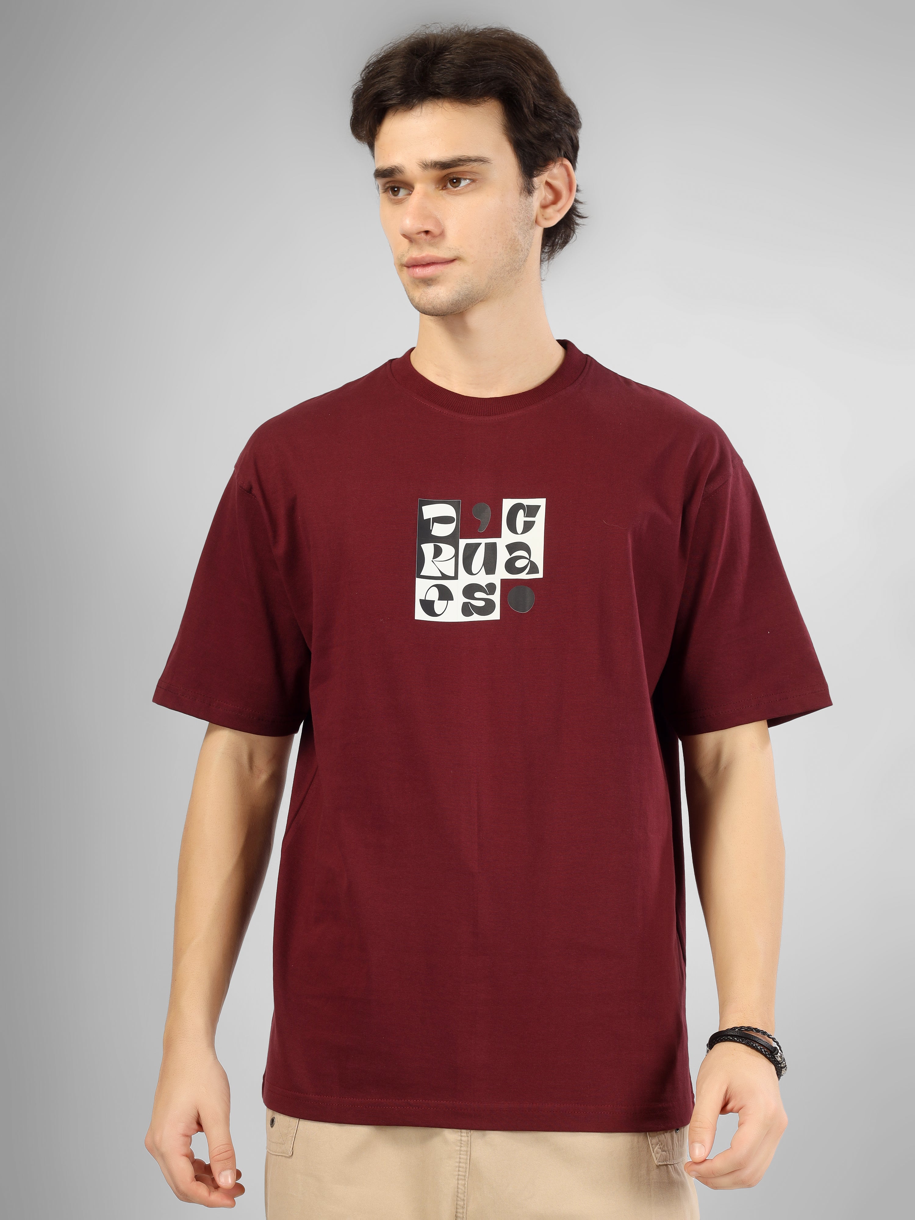 Male model wearing a maroon dcavros T-shirt featuring a black-and-white abstract center logo print, paired with beige pants.