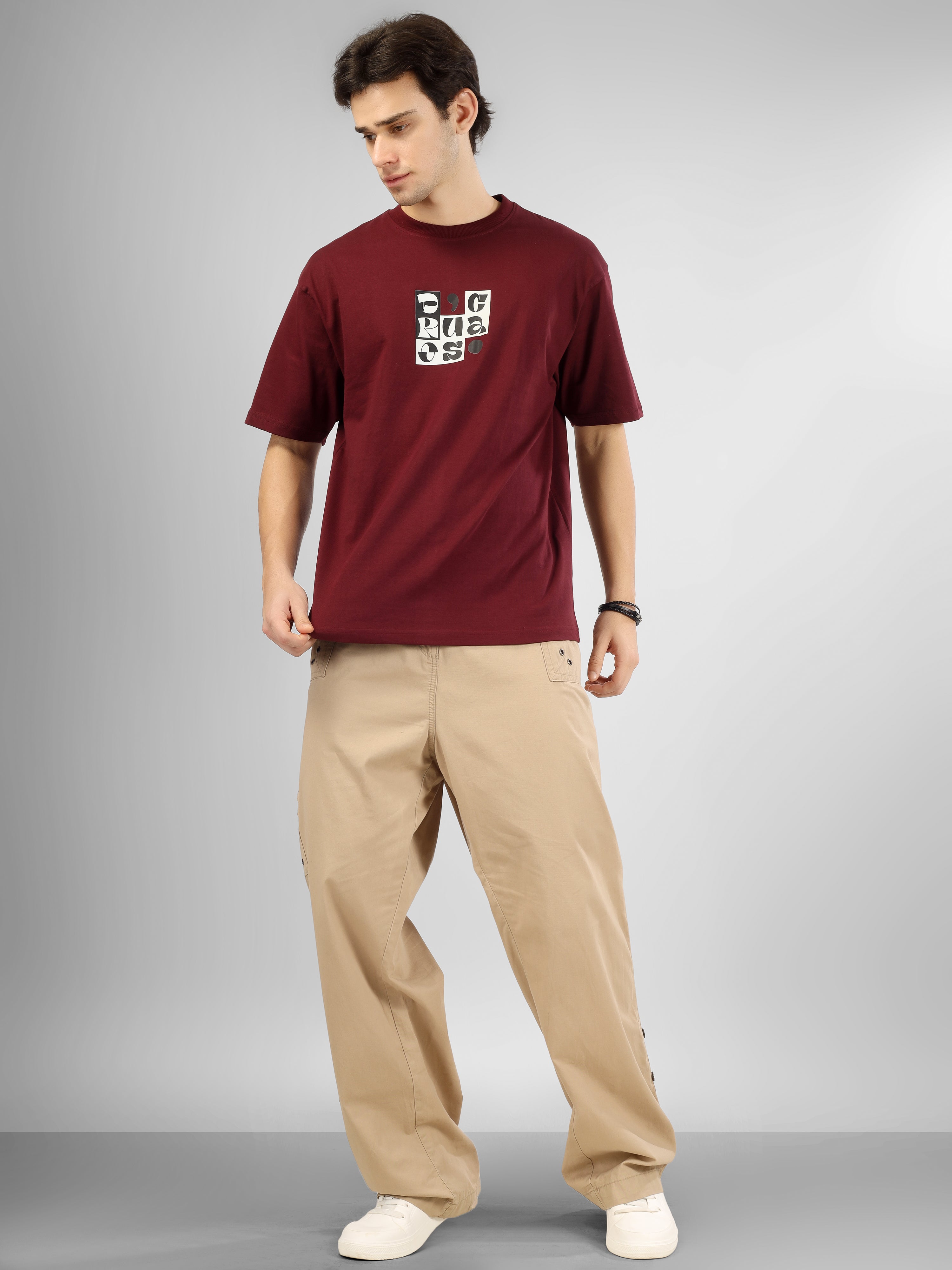 Male model wearing a maroon dcavros T-shirt featuring a black-and-white abstract center logo print, paired with beige pants.