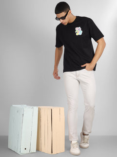 Male model wearing a black oversized dcavros T-shirt with a vibrant multicolor logo on the left chest, paired with white jeans.