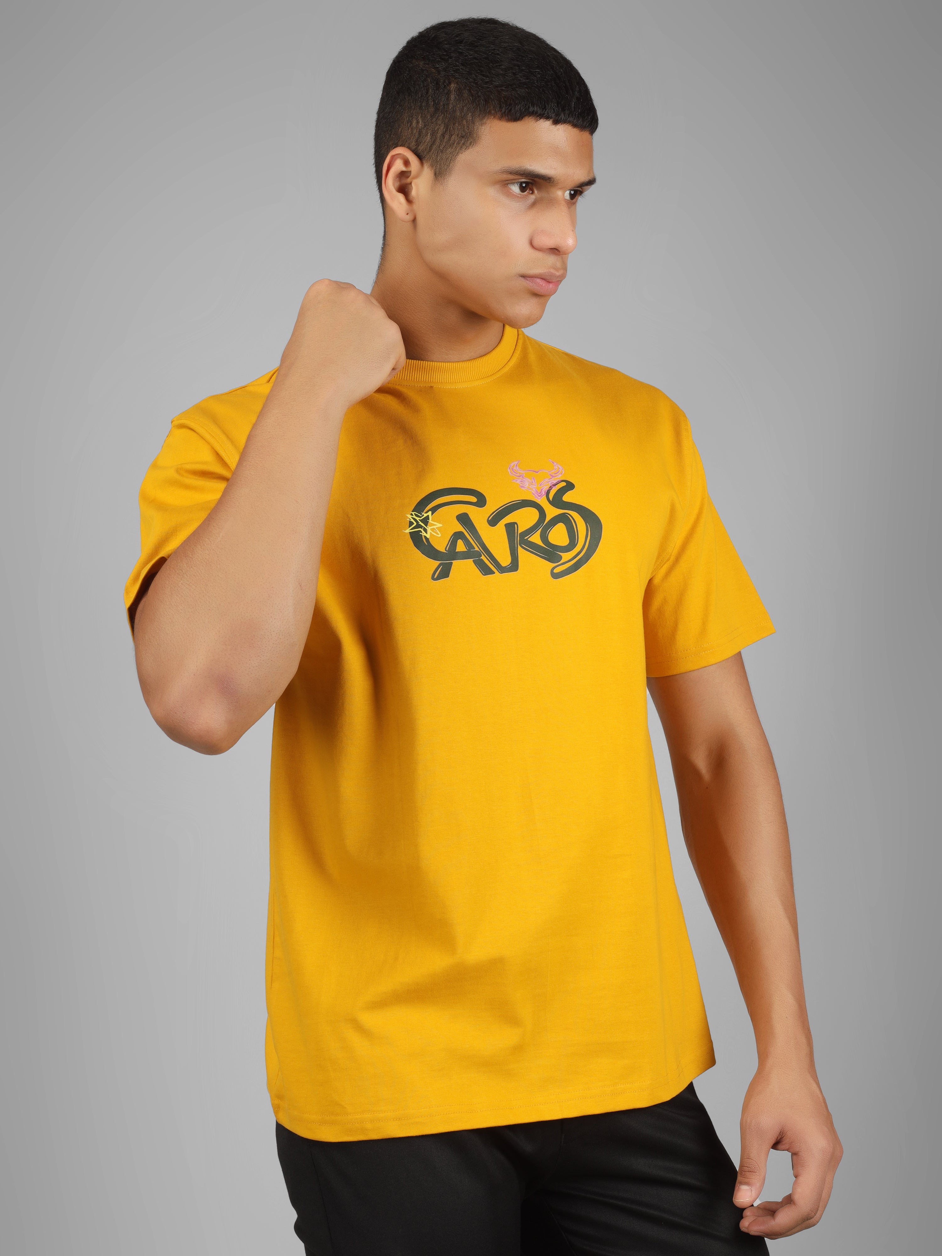 Male model wearing a mustard yellow dcavros unisex T-shirt featuring a bold “Cavros” front logo in black and pink, paired with black pants.