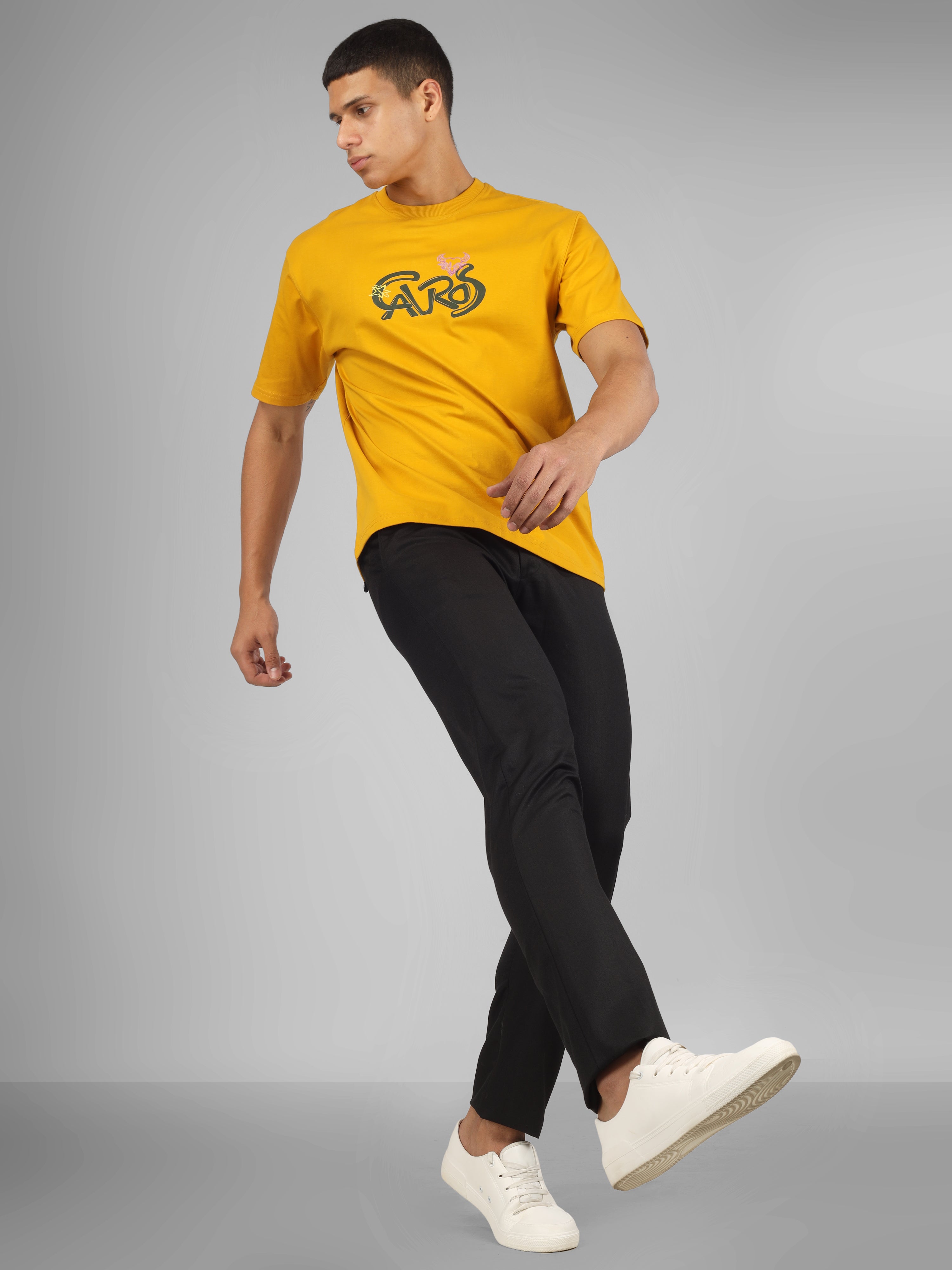 Male model wearing a mustard yellow dcavros unisex T-shirt featuring a bold “Cavros” front logo in black and pink, paired with black pants.