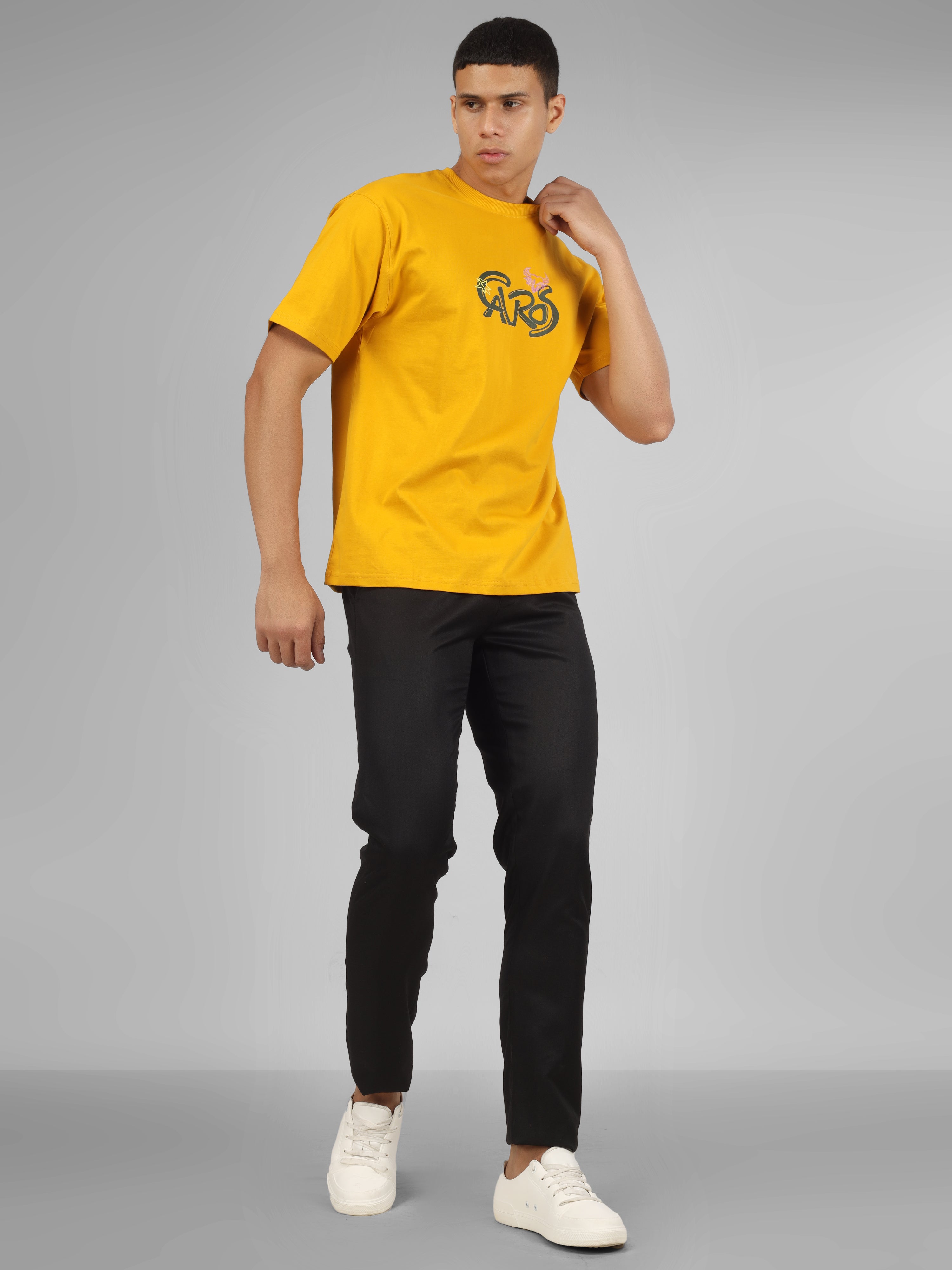 Male model wearing a mustard yellow dcavros unisex T-shirt featuring a bold “Cavros” front logo in black and pink, paired with black pants.