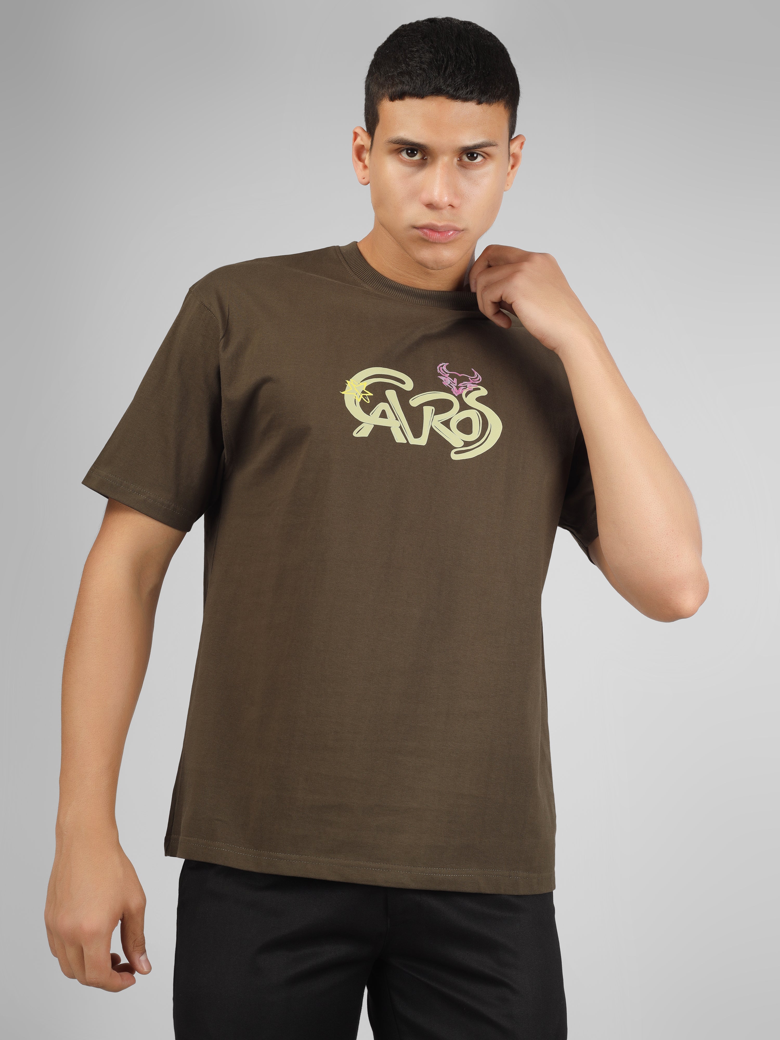 Male model wearing olive green dcavros unisex T-shirt with a yellow and pink "Cavros" bull logo on the chest, styled with black pants.