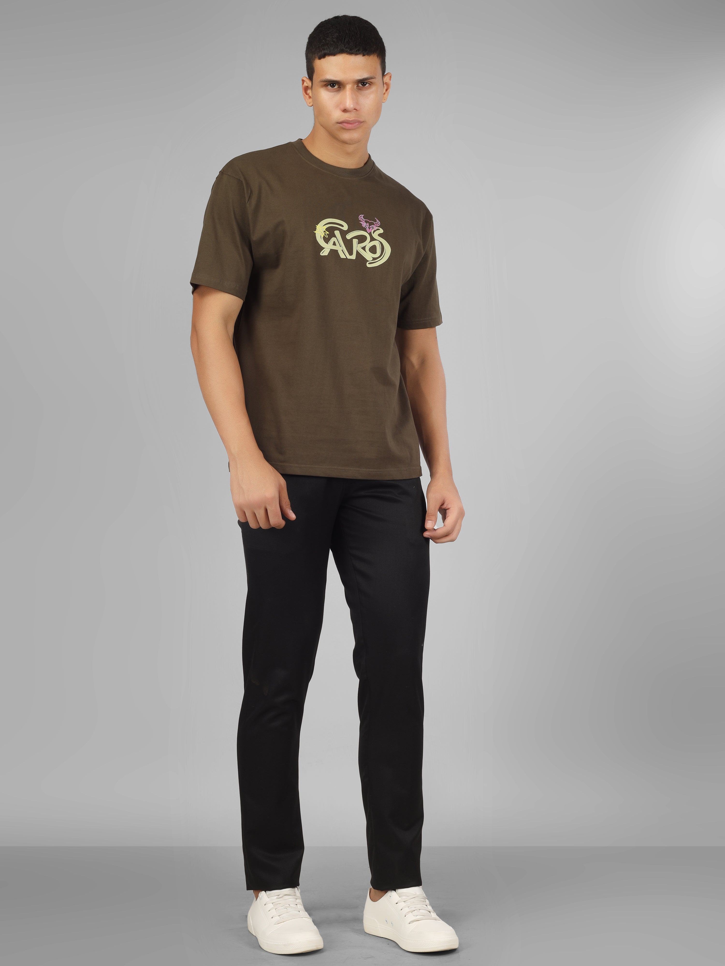 Male model wearing olive green dcavros unisex T-shirt with a yellow and pink "Cavros" bull logo on the chest, styled with black pants.