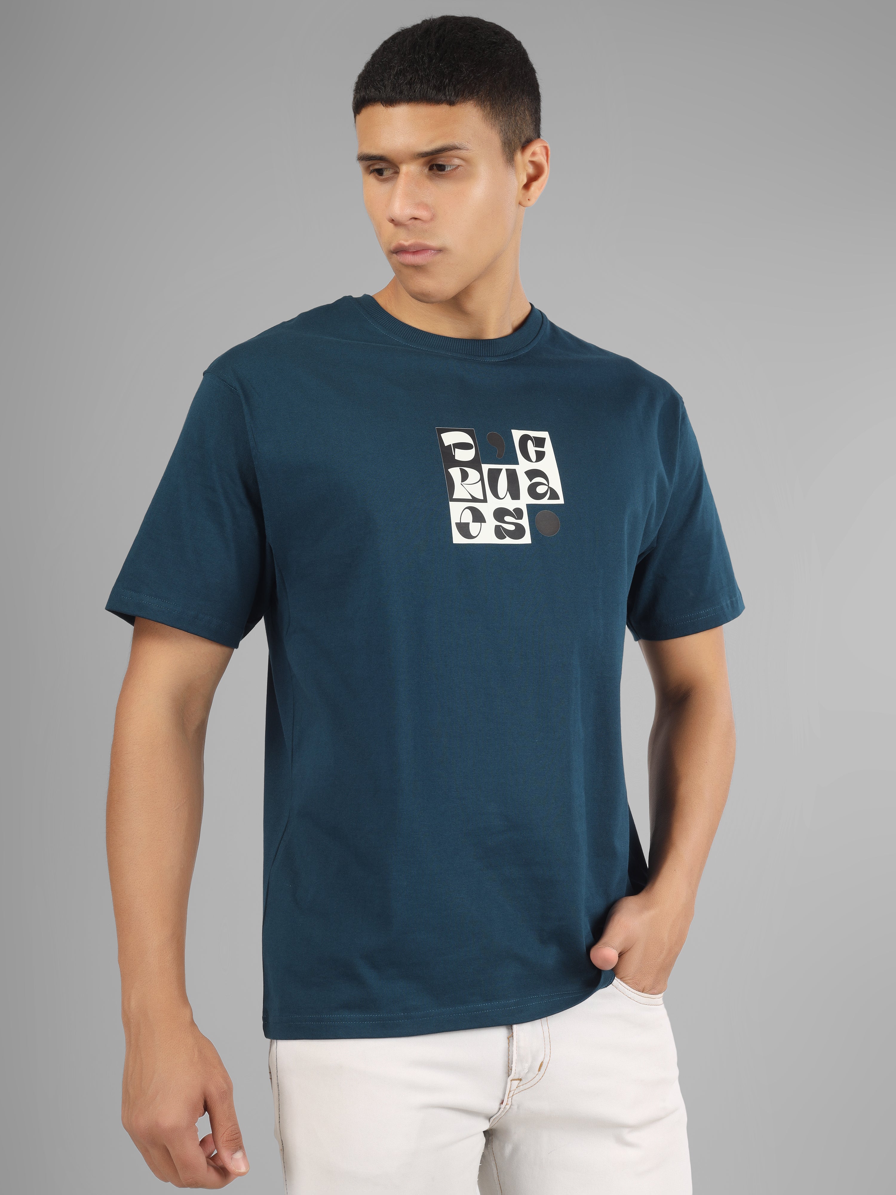 Male model wearing a petrol blue dcavros T-shirt with a bold abstract central logo print in black and white, paired with white jeans.