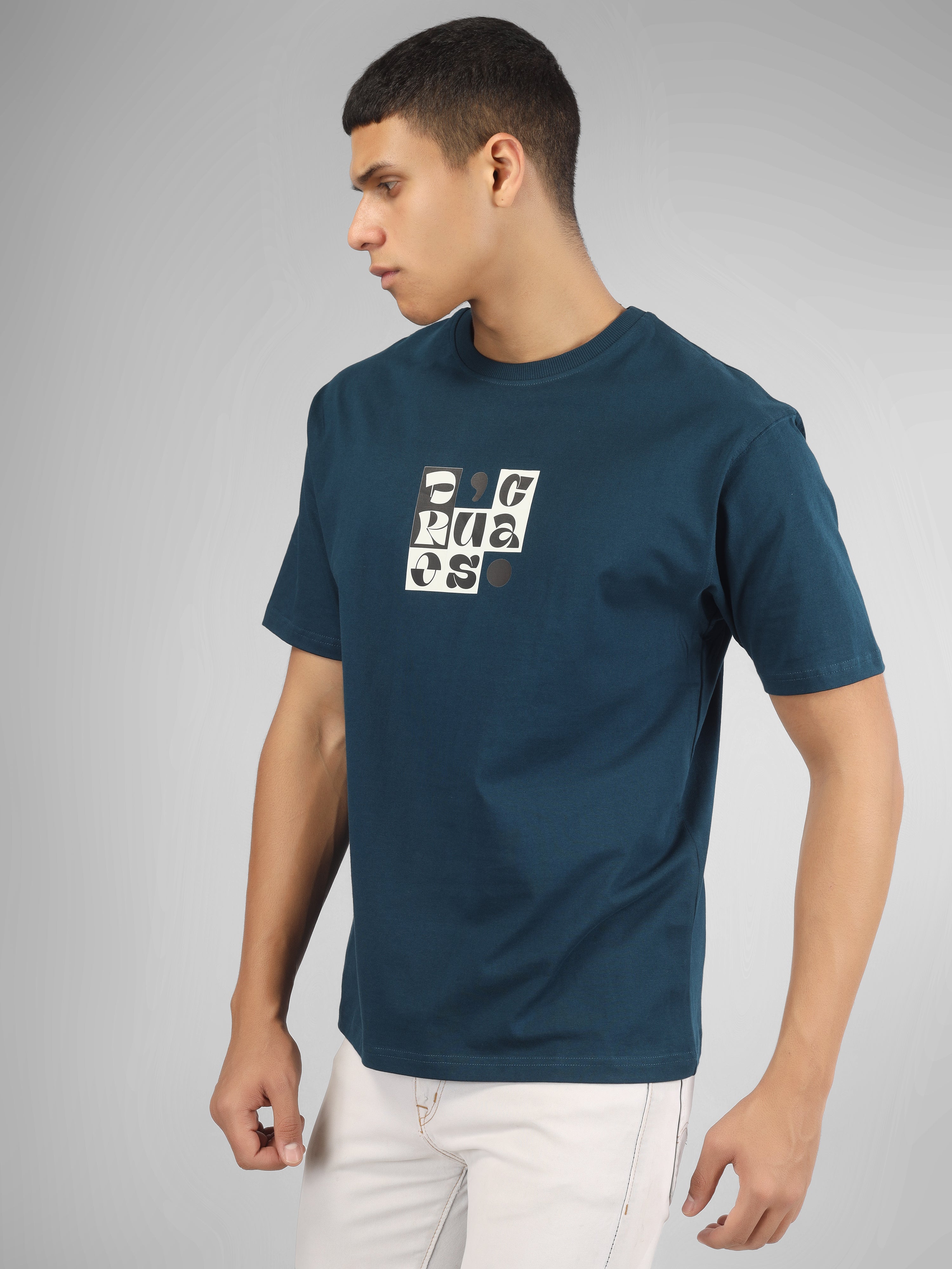 Male model wearing a petrol blue dcavros T-shirt with a bold abstract central logo print in black and white, paired with white jeans.