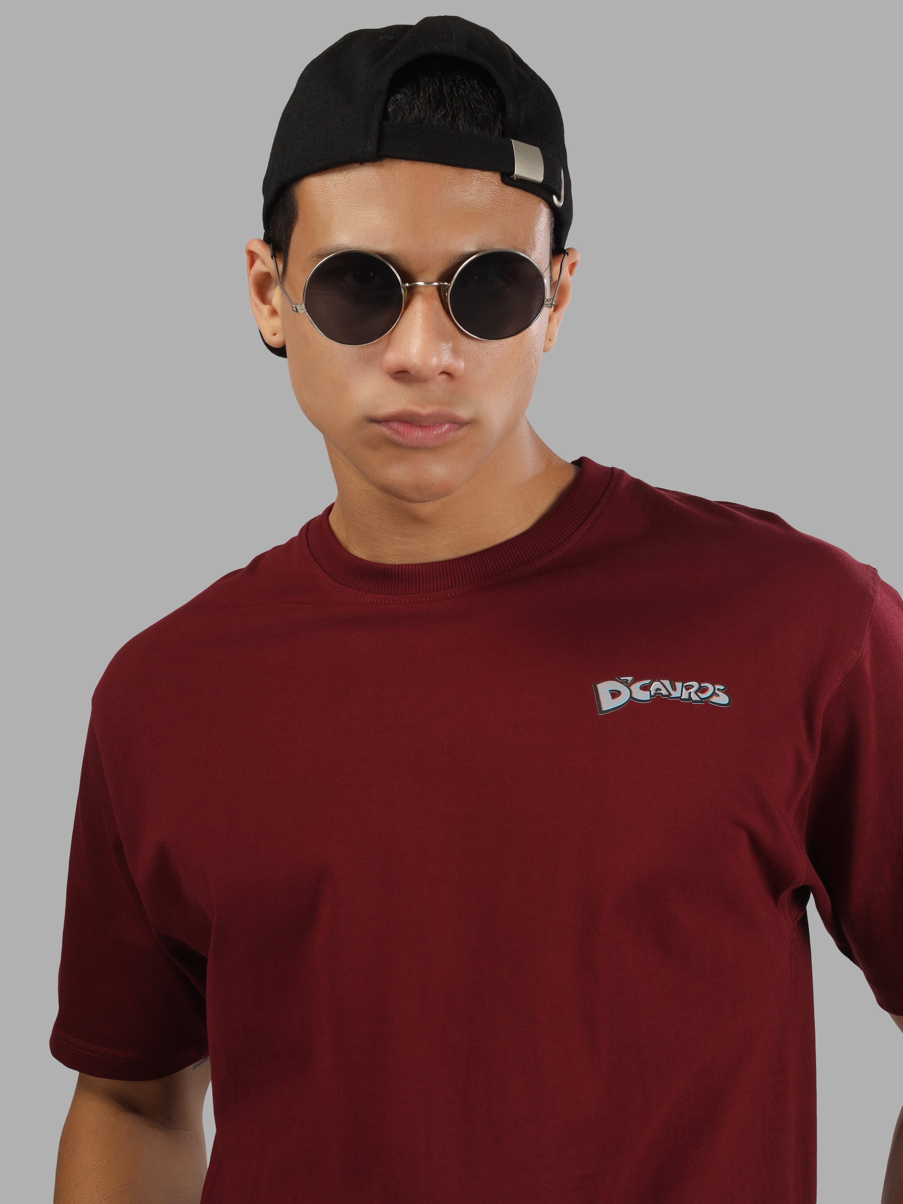 Male model wearing a maroon dcavros graphic T-shirt with a spiral text logo on the back and relaxed fit, styled with beige jeans.