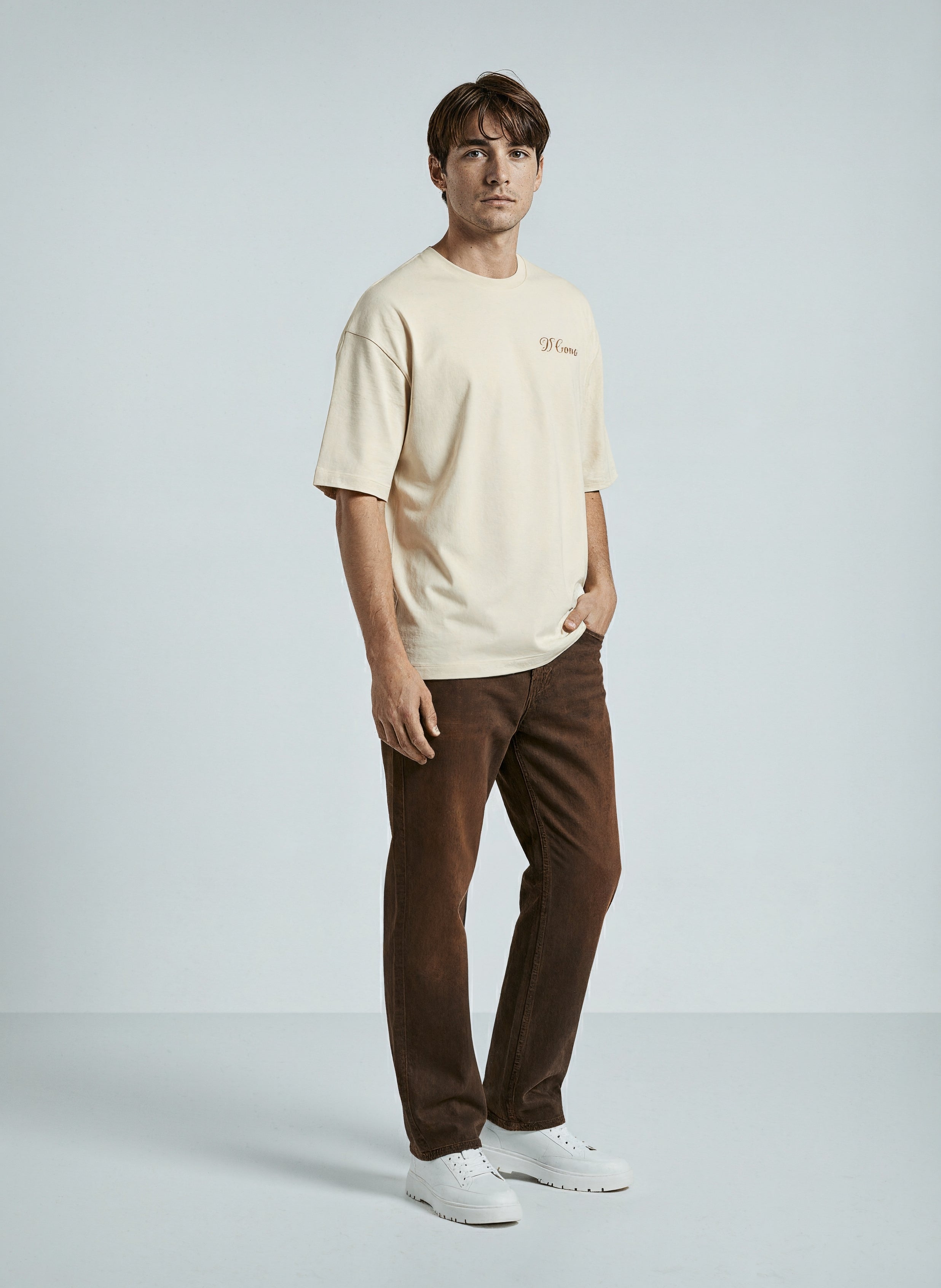 A model wearing the Skyline Chaser Unisex Oversized Tee in beige, paired with brown pants and white sneakers.