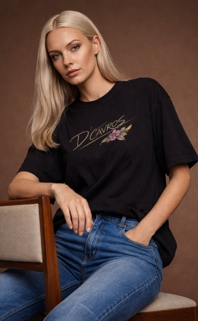 Woman wearing a black t-shirt with a floral design and text, sitting on a chair against a brown background.