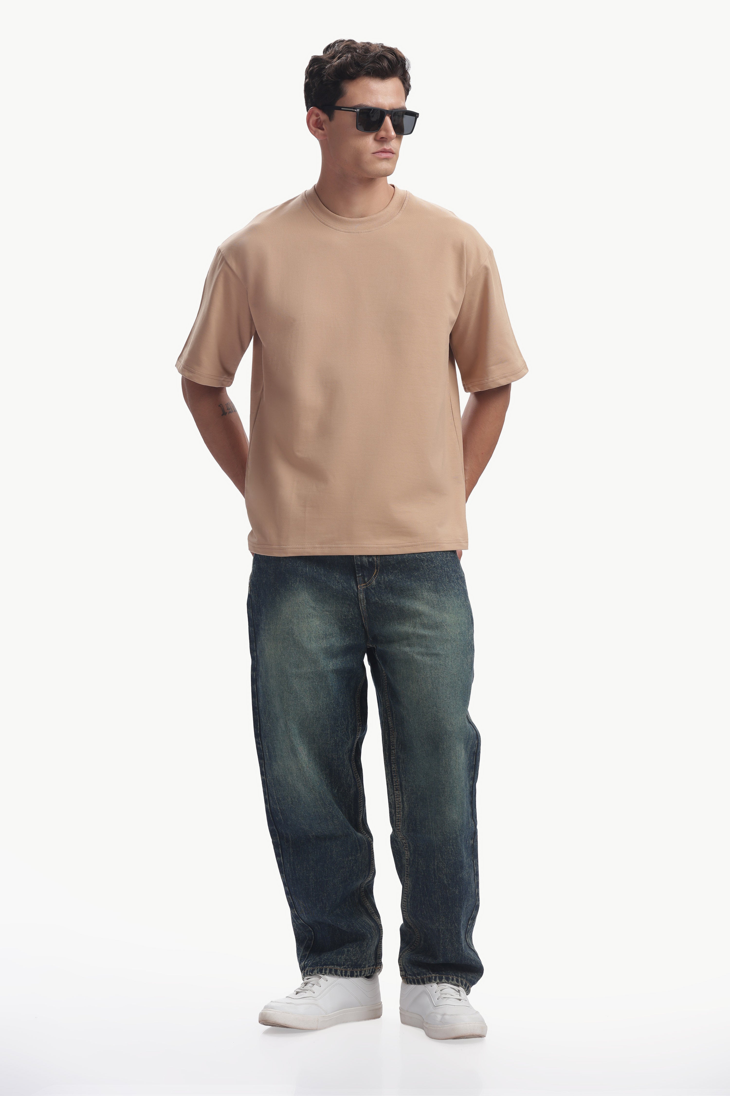 Man wearing an oversized fit focal point t-shirt in beige color paired with blue jeans and sunglasses.