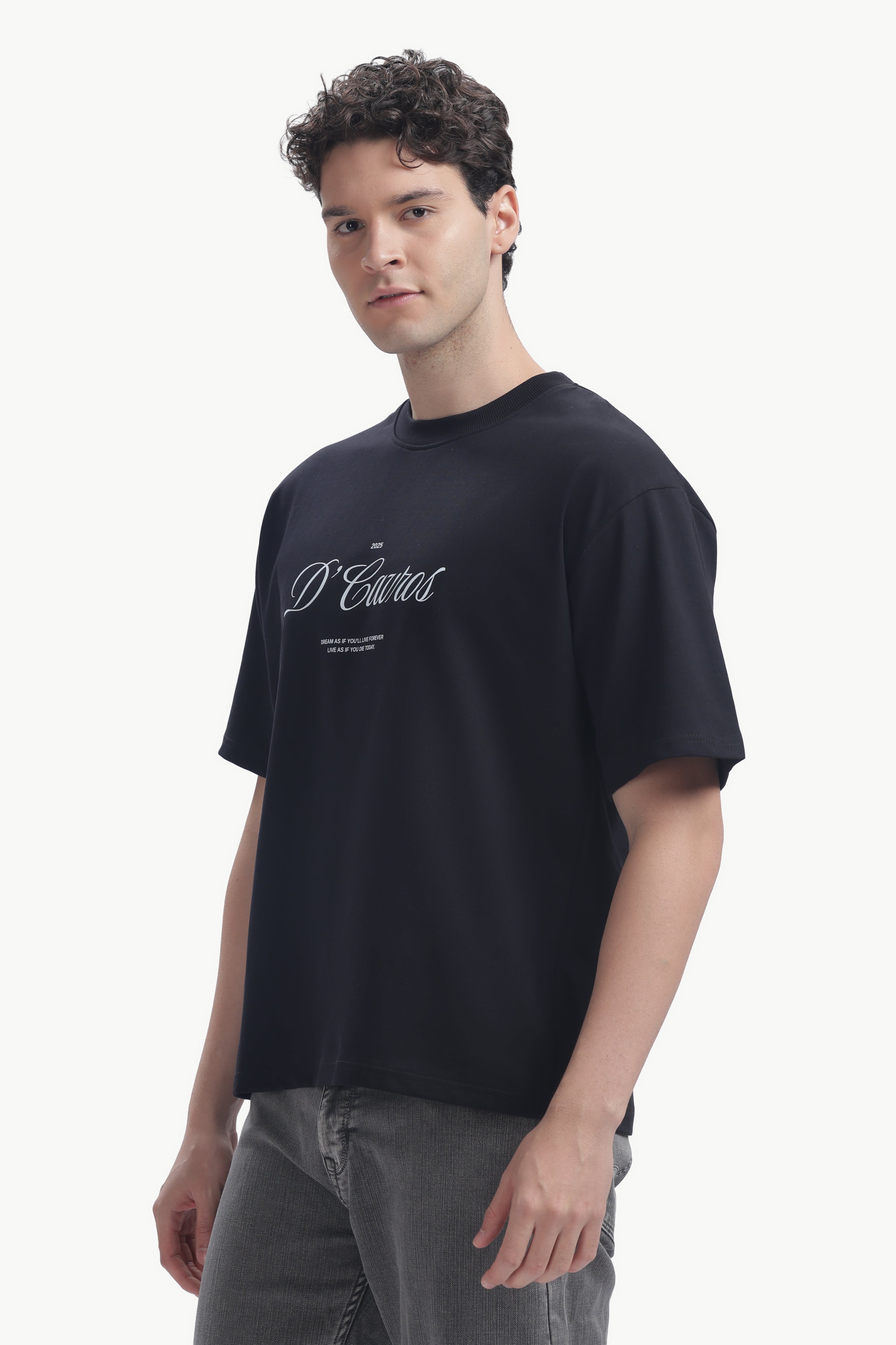 Model wearing a Classic Loose Fit Typography T-Shirt in black with bold D’Cavros script print.
