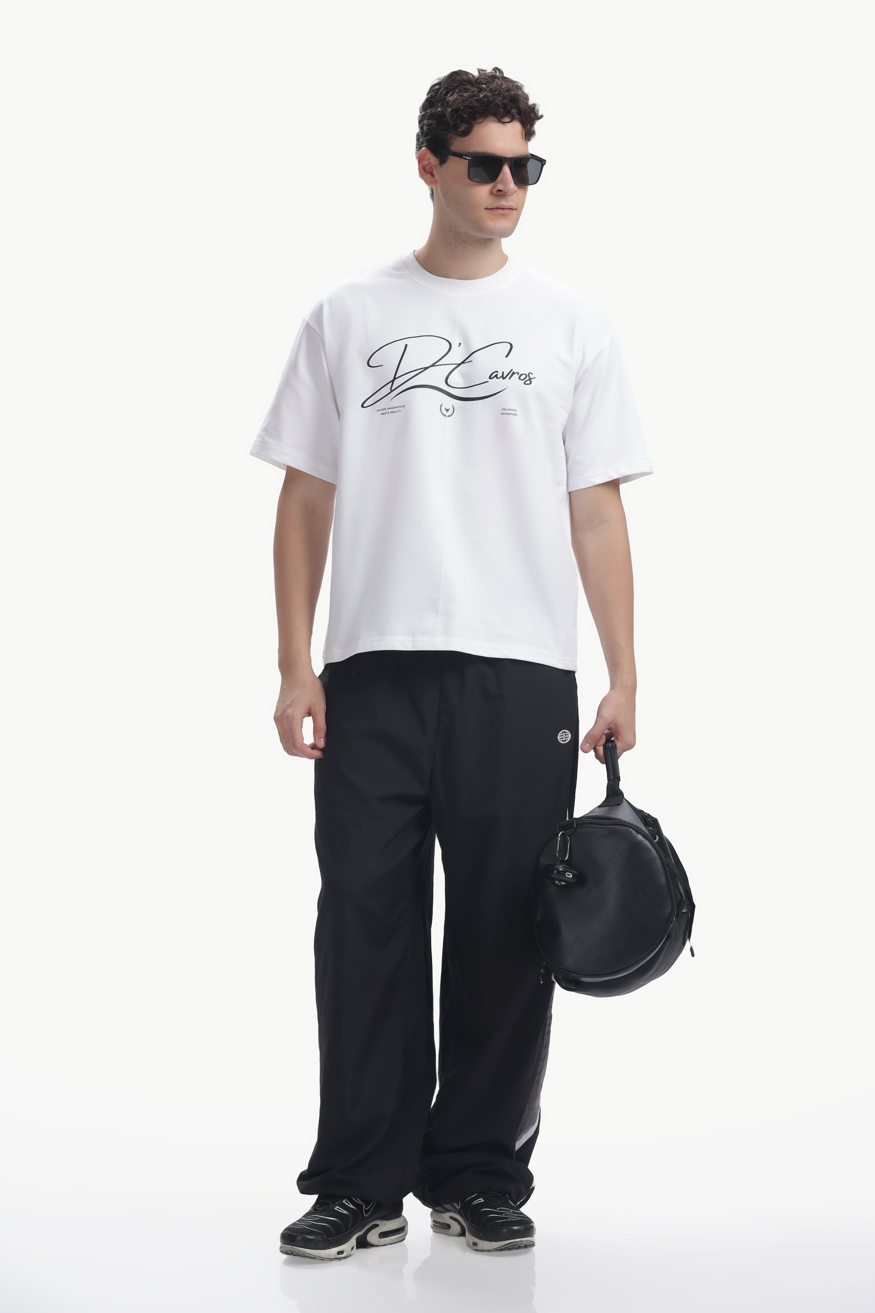 Model wearing Community Capsule Graphics Tee with relaxed fit and signature typography, paired with black pants and sunglasses.