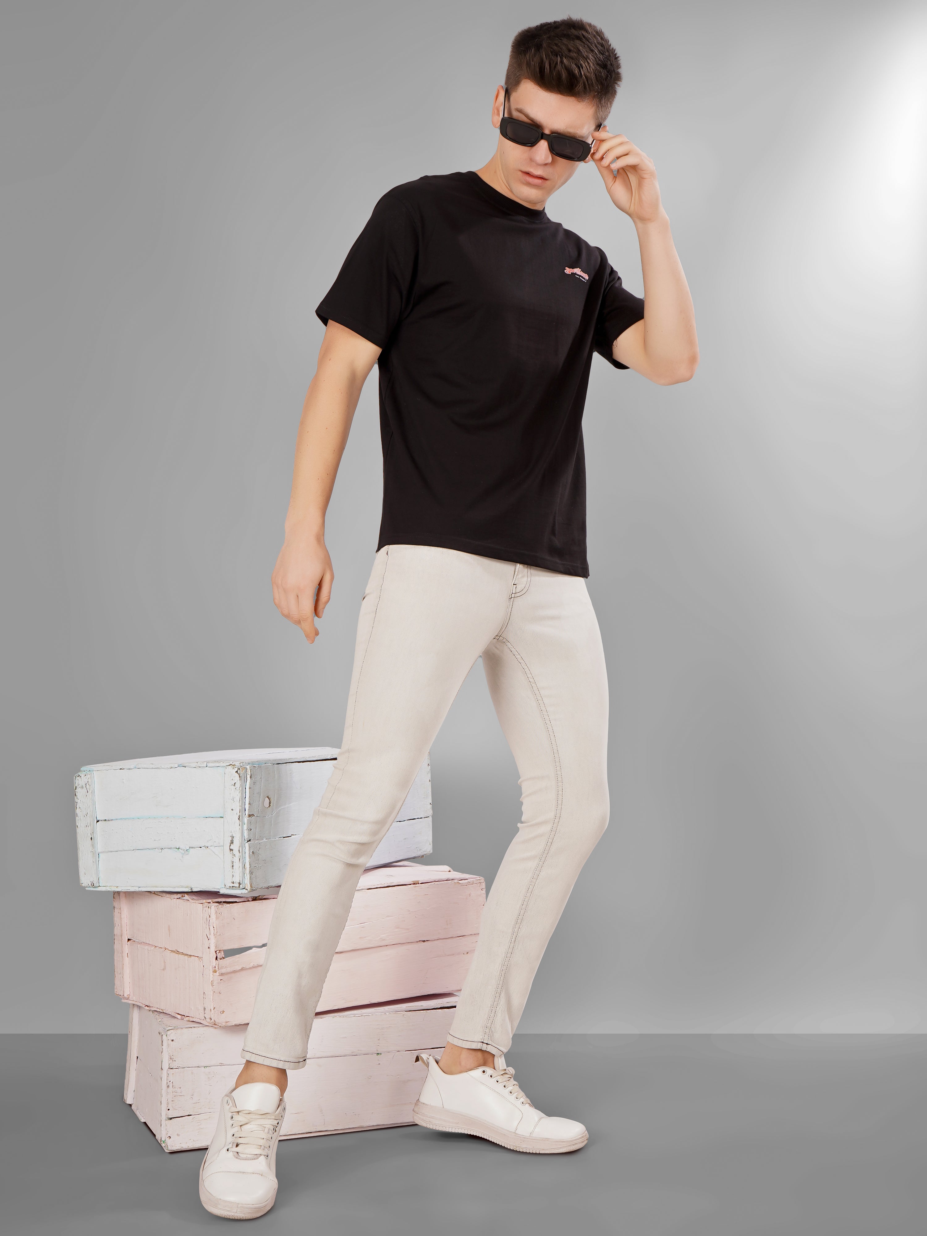 Man wearing Sports Car Oversized T-Shirt with sunglasses, standing in front of colorful boxes.