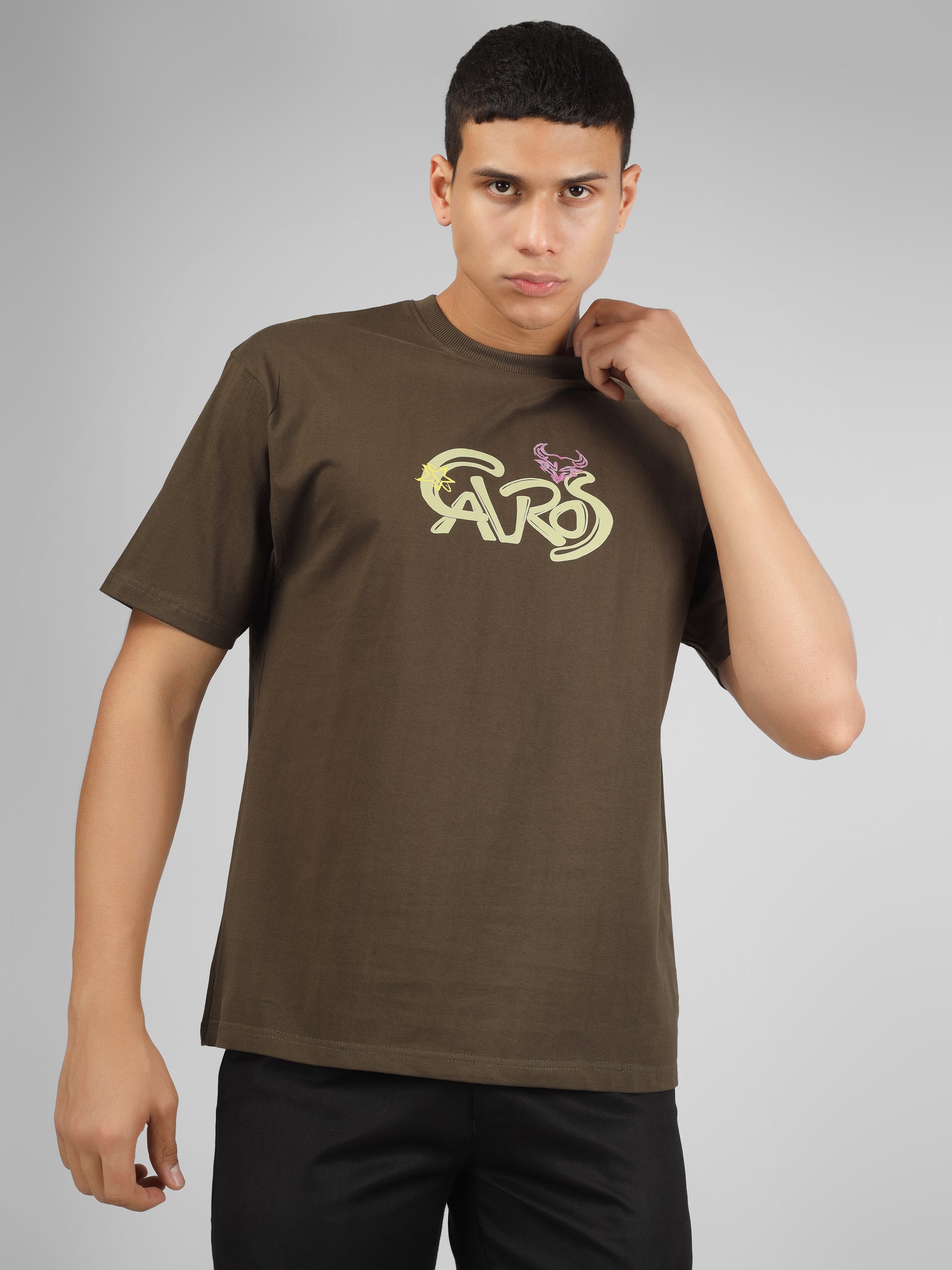Male model wearing olive green dcavros unisex T-shirt with a yellow and pink "Cavros" bull logo on the chest, styled with black pants.