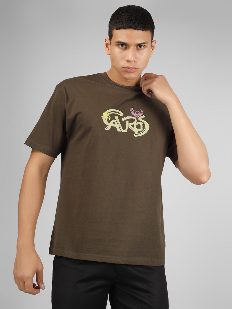 Male model wearing olive green dcavros unisex T-shirt with a yellow and pink "Cavros" bull logo on the chest, styled with black pants.