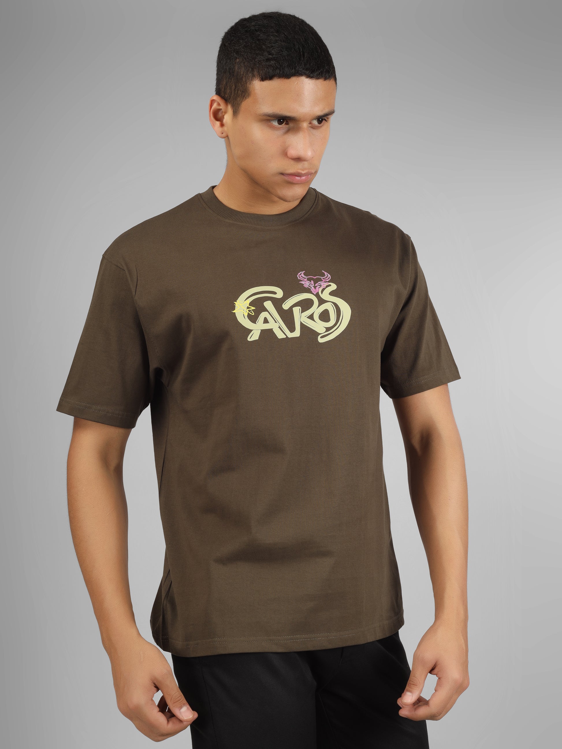 Male model wearing olive green dcavros unisex T-shirt with a yellow and pink "Cavros" bull logo on the chest, styled with black pants.