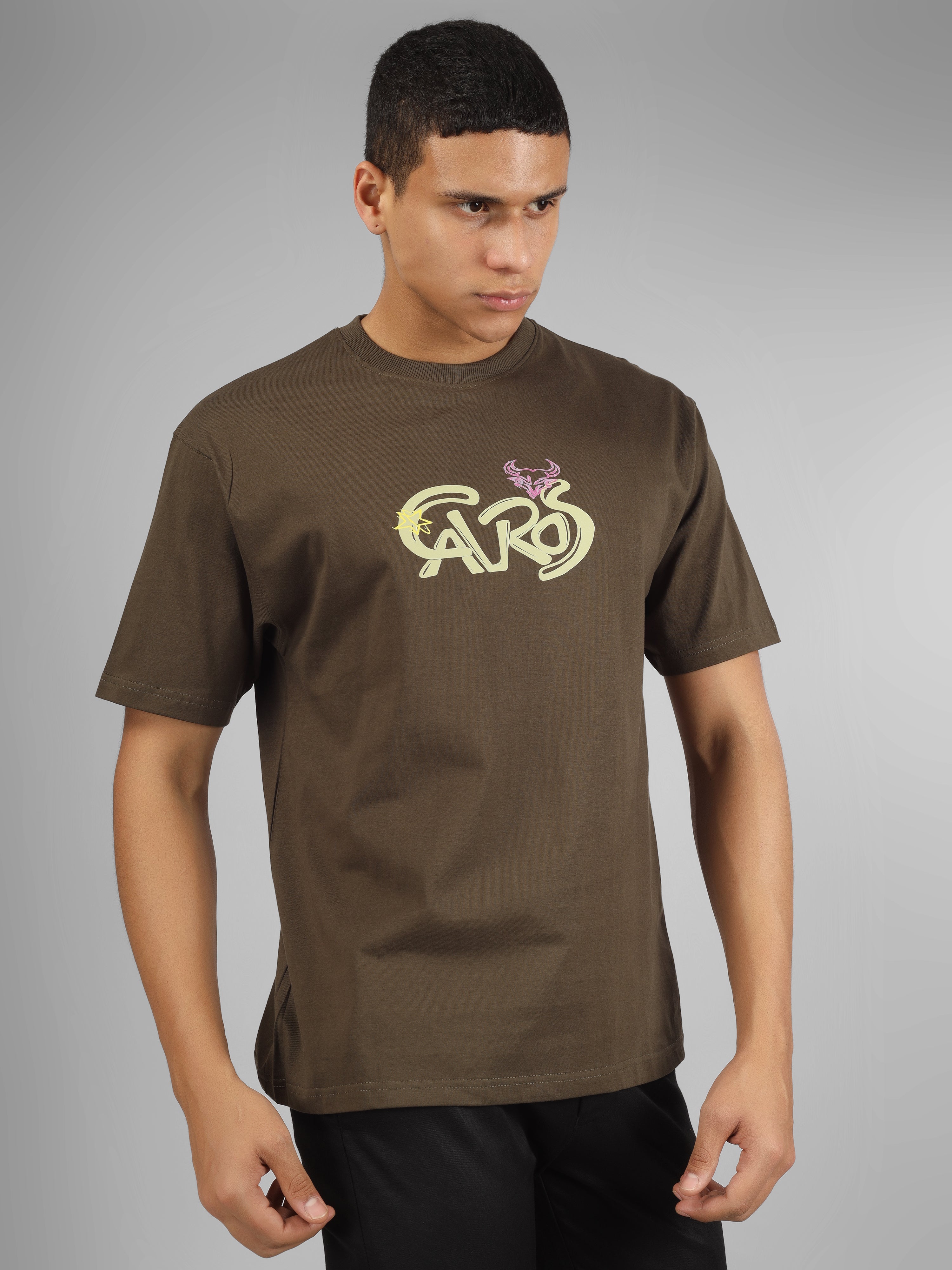 Male model wearing olive green dcavros unisex T-shirt with a yellow and pink "Cavros" bull logo on the chest, styled with black pants.