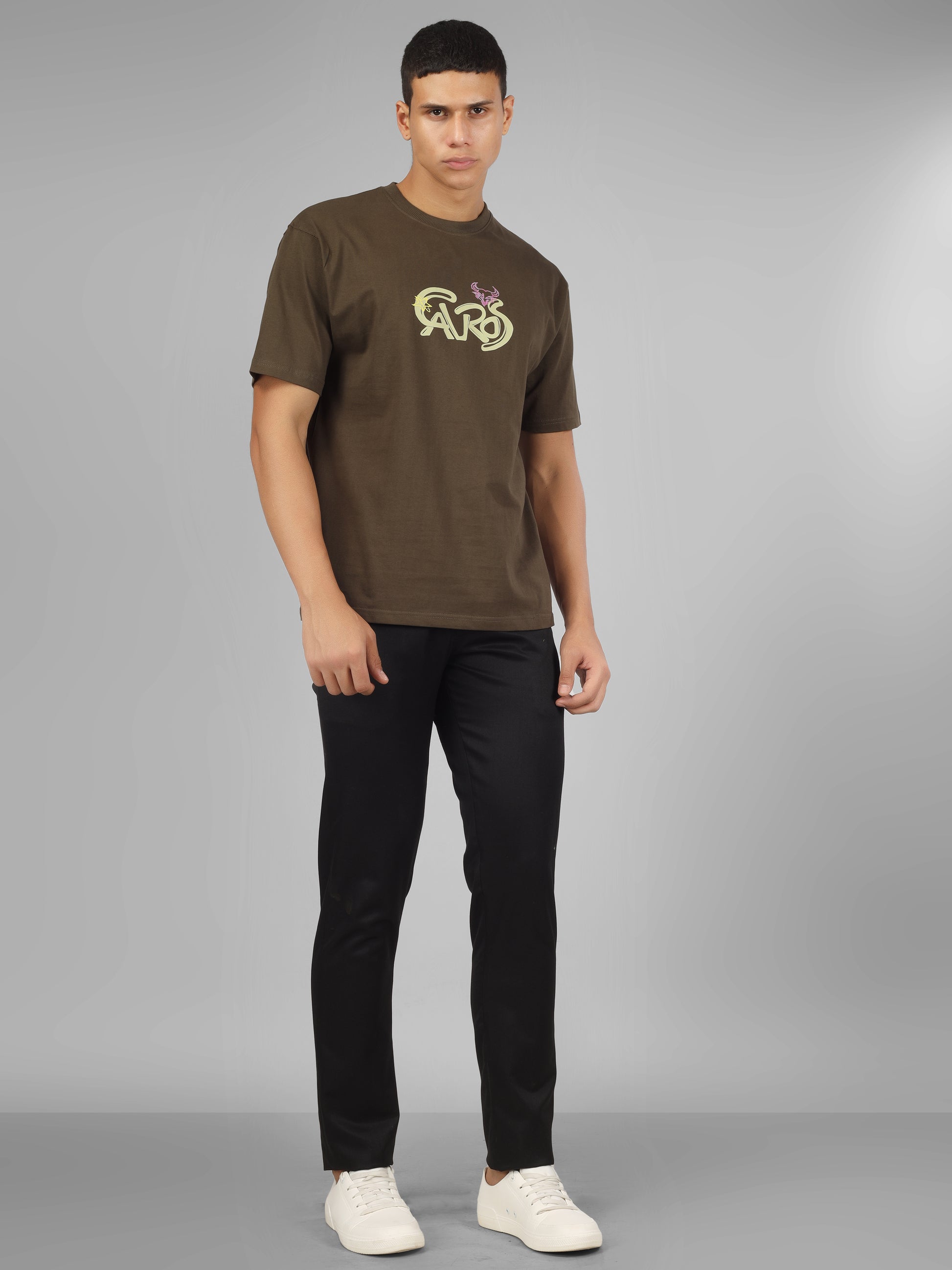 Male model wearing olive green dcavros unisex T-shirt with a yellow and pink "Cavros" bull logo on the chest, styled with black pants.