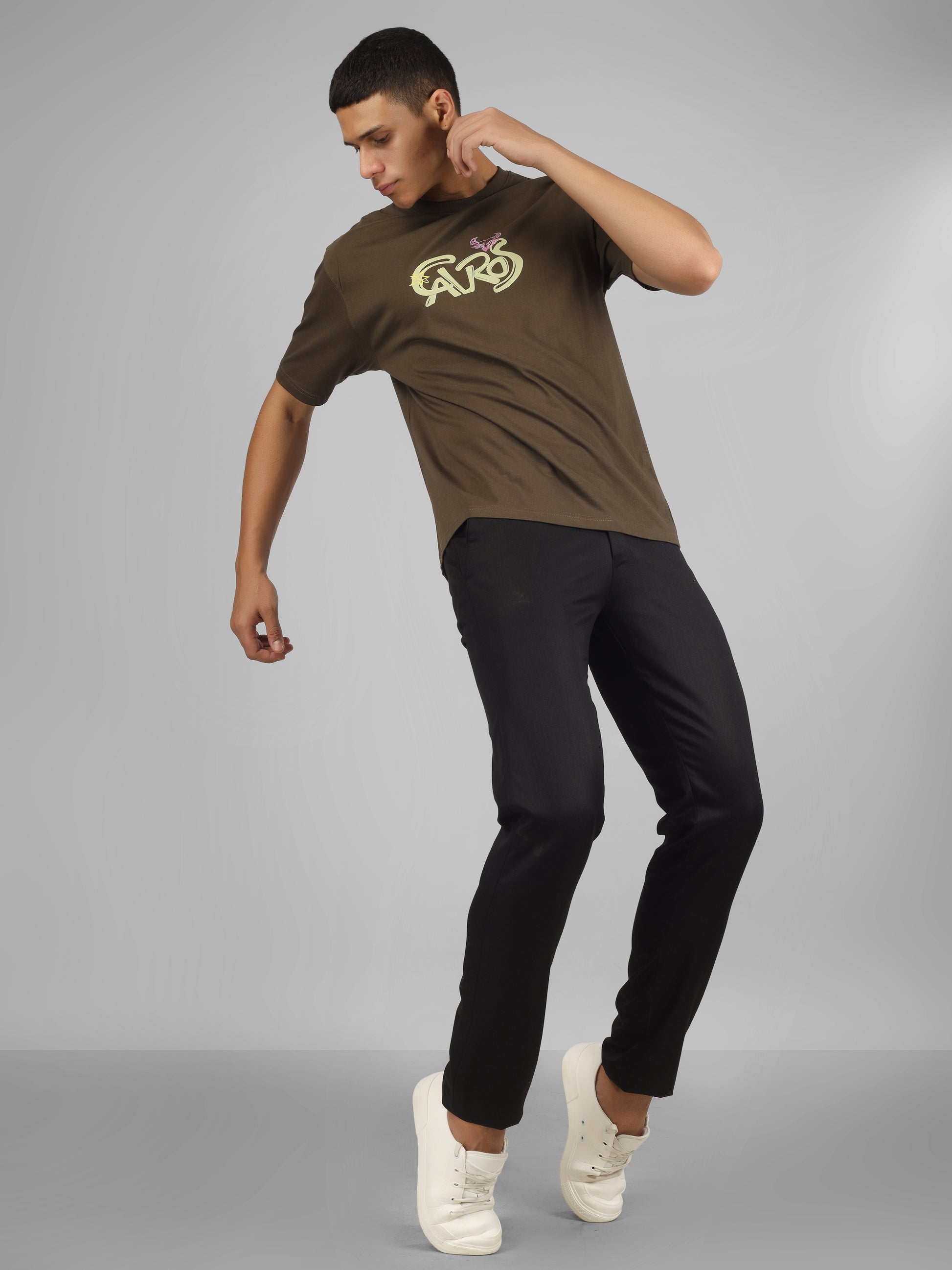 Male model wearing olive green dcavros unisex T-shirt with a yellow and pink "Cavros" bull logo on the chest, styled with black pants.
