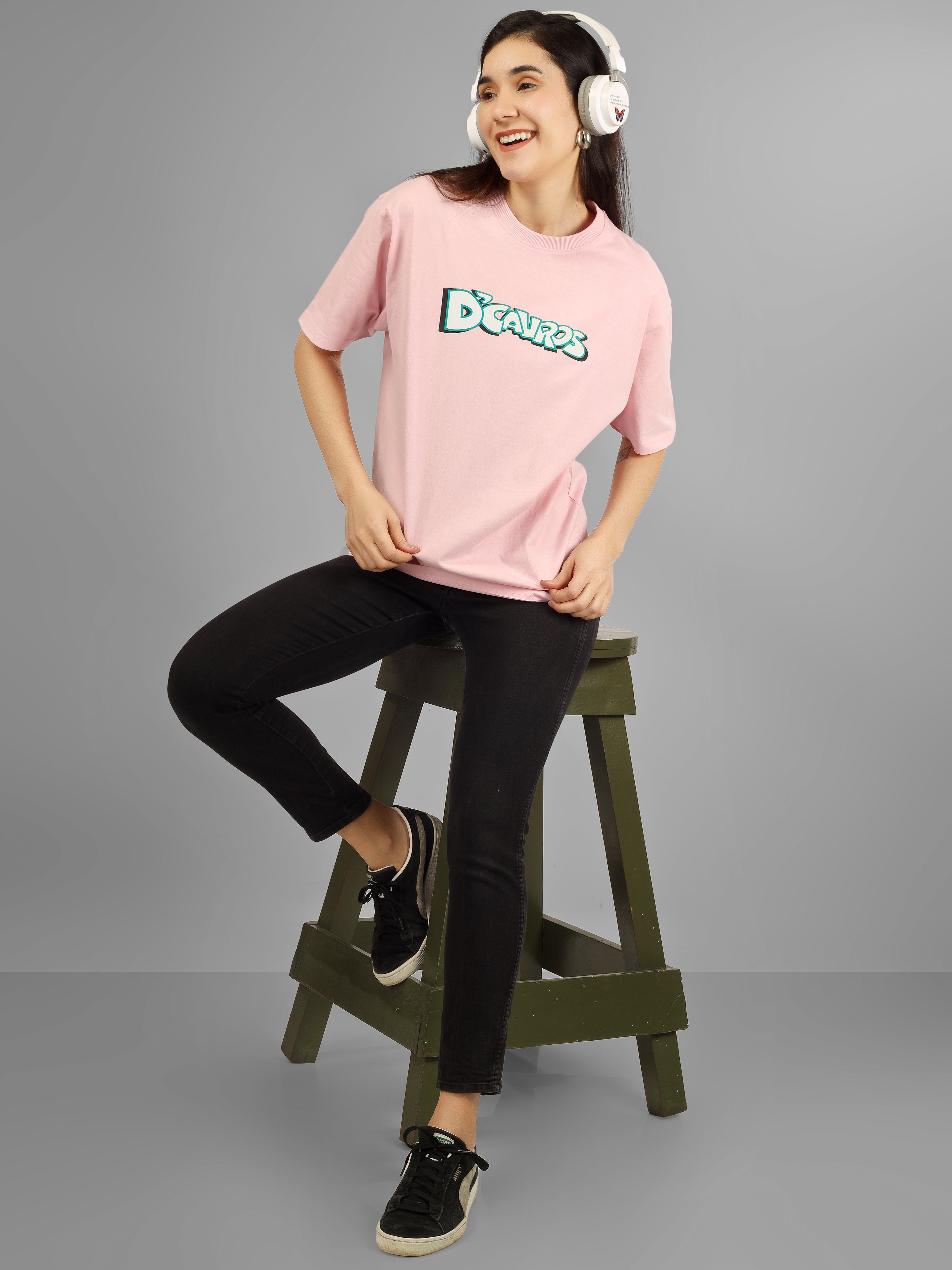 Solid Graphic D'Cavros Tee Womens model wearing a pink tee and black pants while posing on a stool.